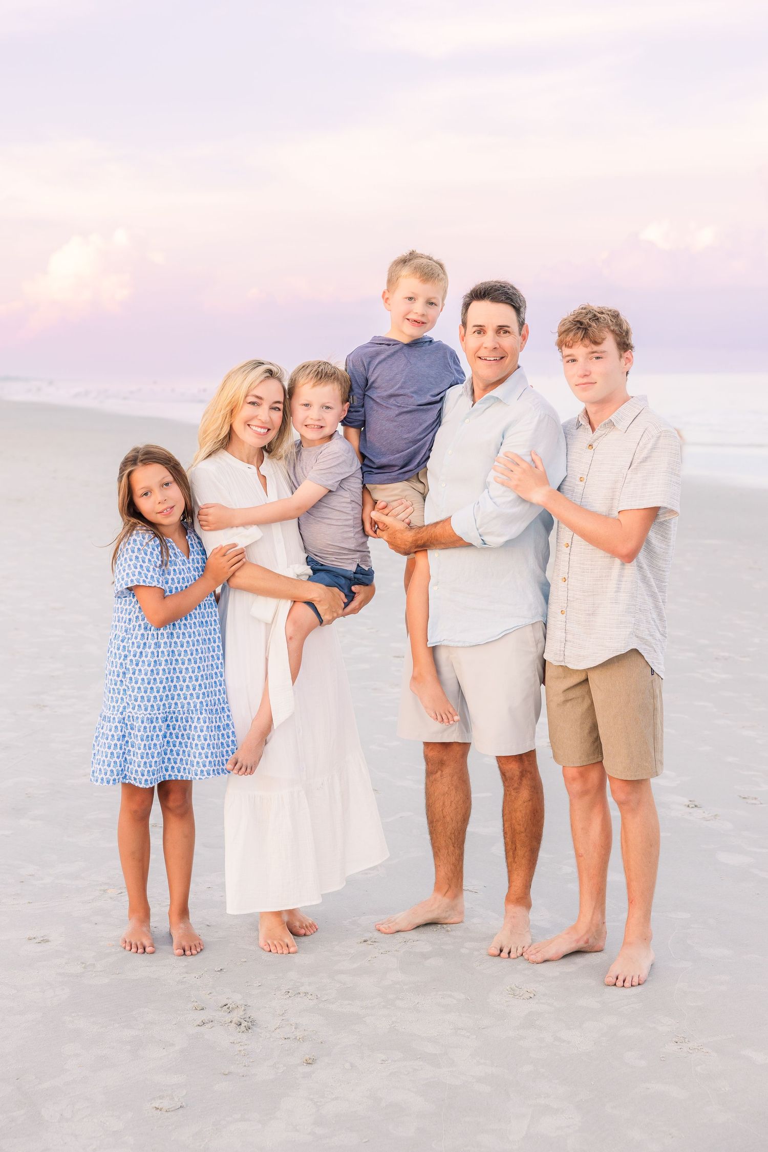 Family of six posing together barefoot on a beach during golden hour.