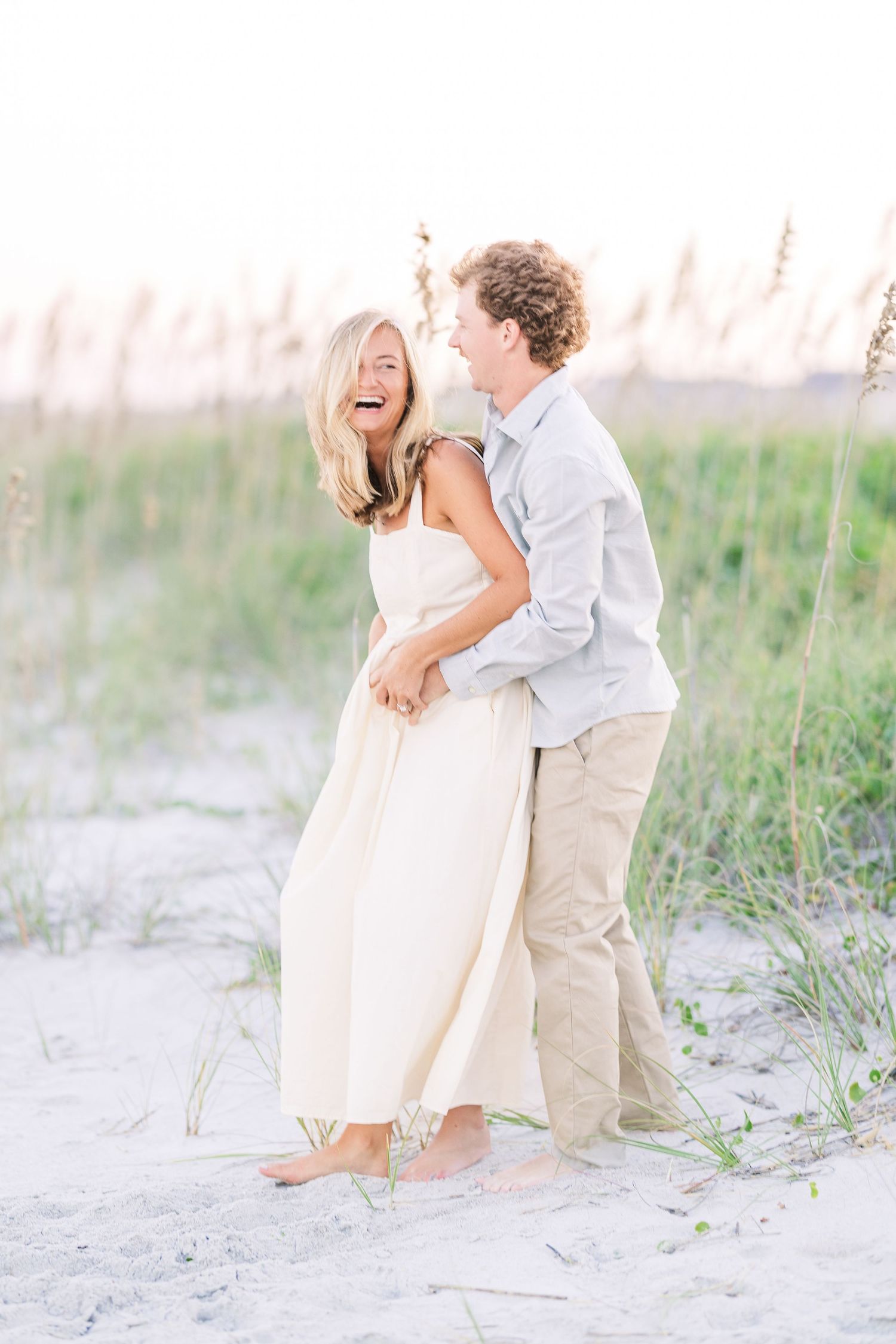 Couple in casual beach attire sharing tender moments among coastal dunes.