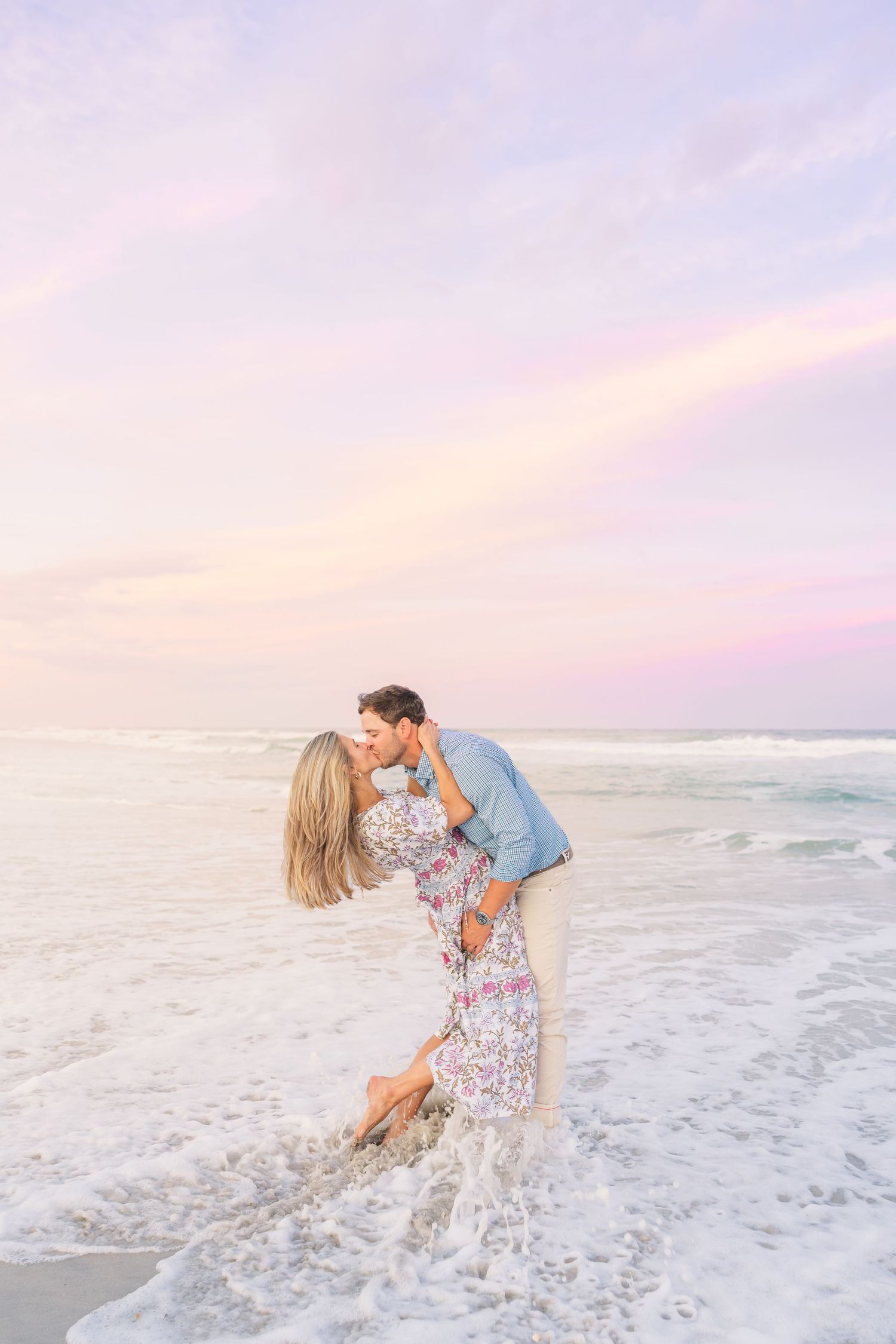 A romantic couple embraces in the ocean waves during a dreamy pink sunset.