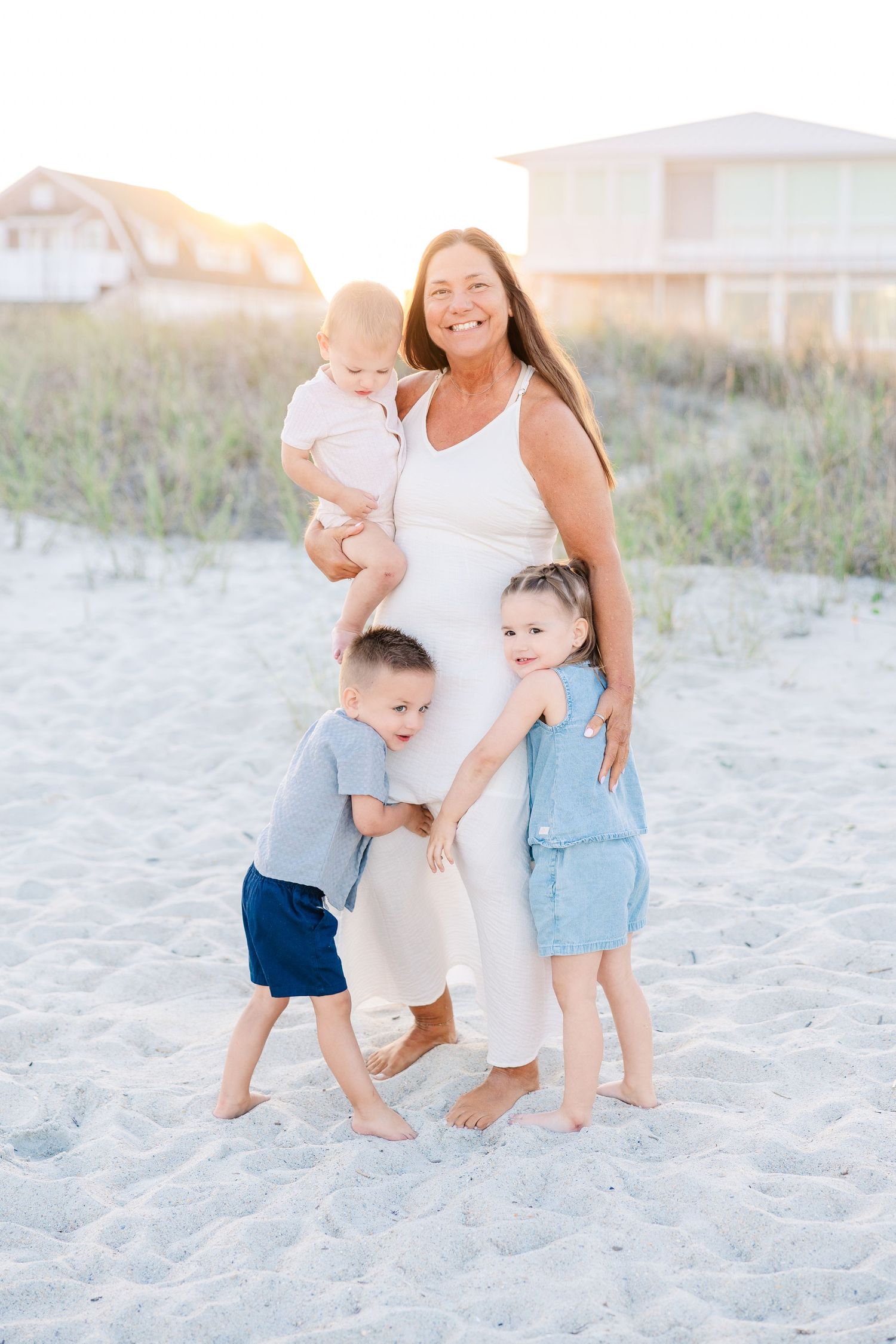 Happy grandmother holding baby surrounded by two young grandchildren on a sunny sandy beach.