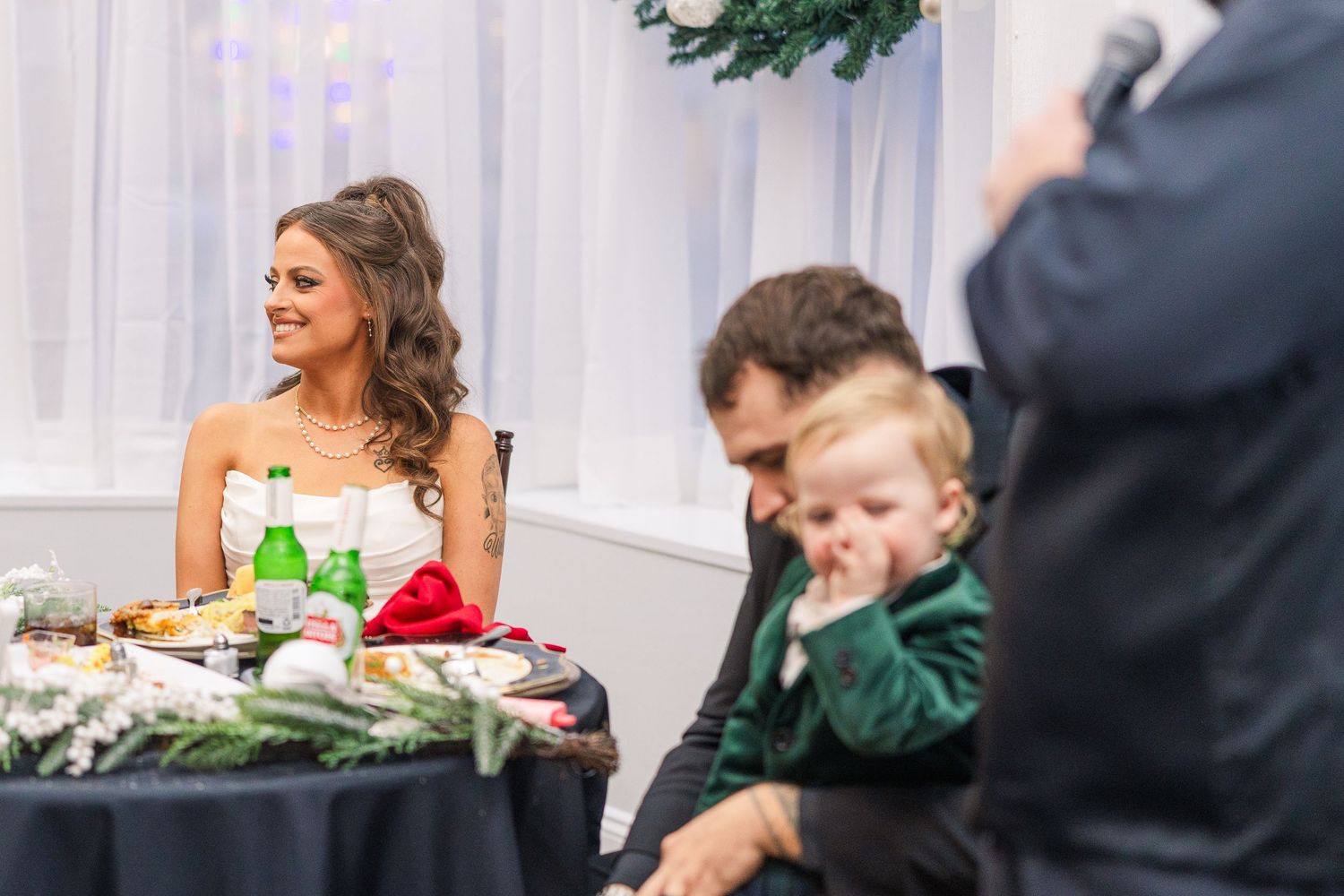Wedding reception guests enjoying a festive dinner with holiday decorations and greenery in the background.