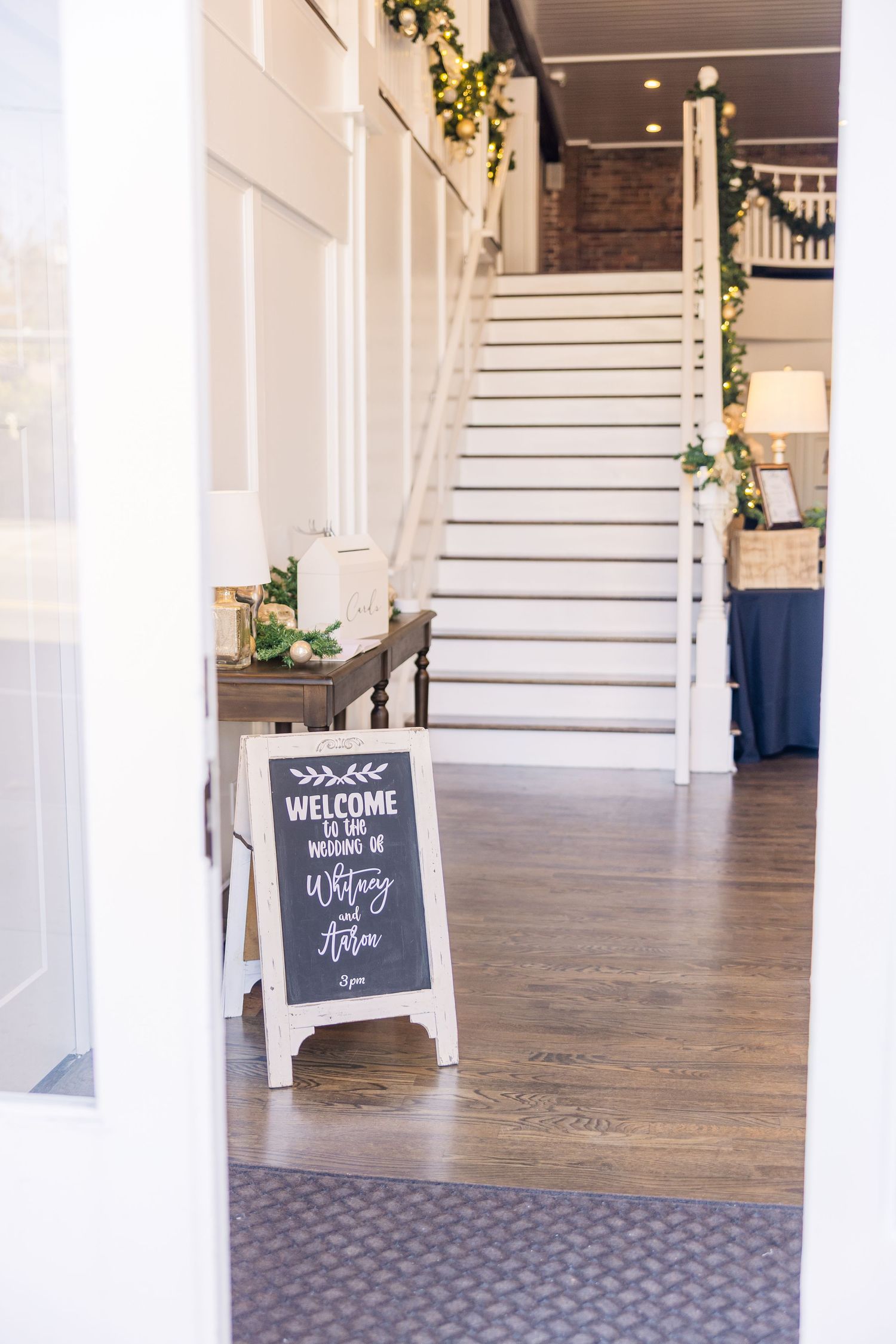 A bright indoor venue space with white columns and wooden floors featuring welcome signs.