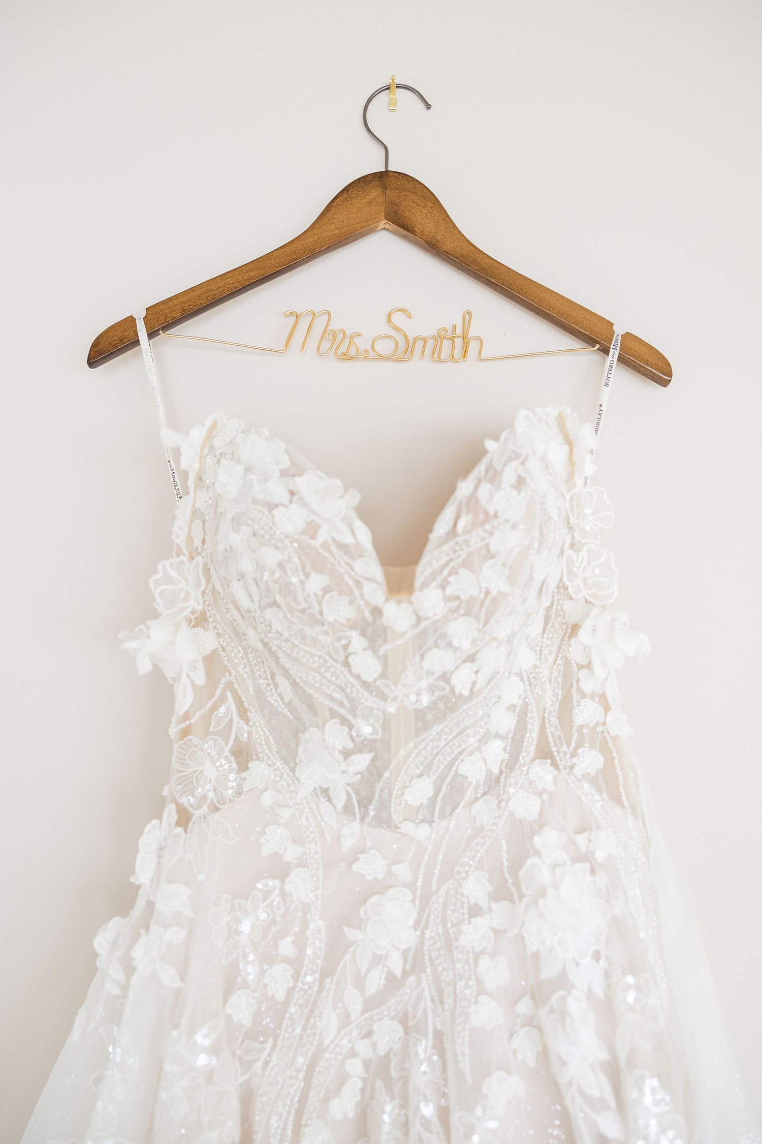 Elegant white lace wedding dress with floral appliques hanging on wooden hanger with personalized name wilmington wedding photographer