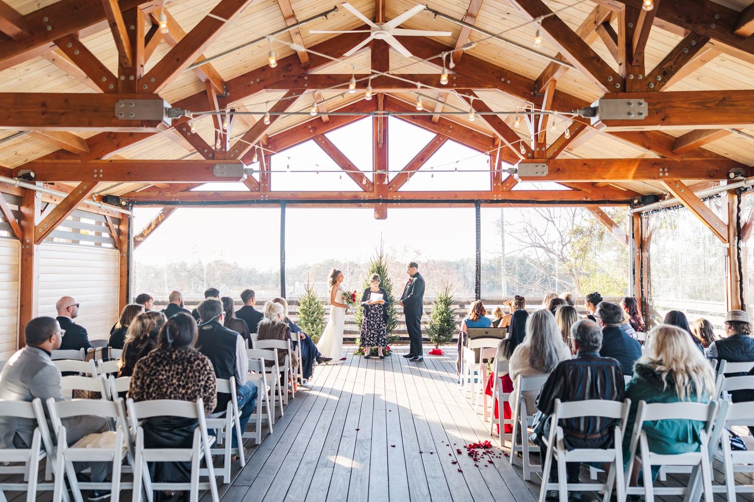 Wedding ceremony taking place in a rustic wooden pavilion with exposed beams and white chairs overlooking scenic views.