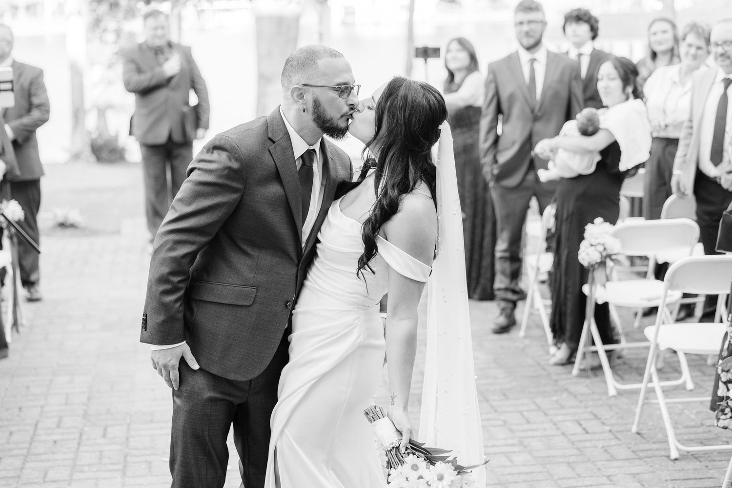 Black and white photo of wedding ceremony with guests seated outdoors wedding groom bride lake Gaston photographer light airy