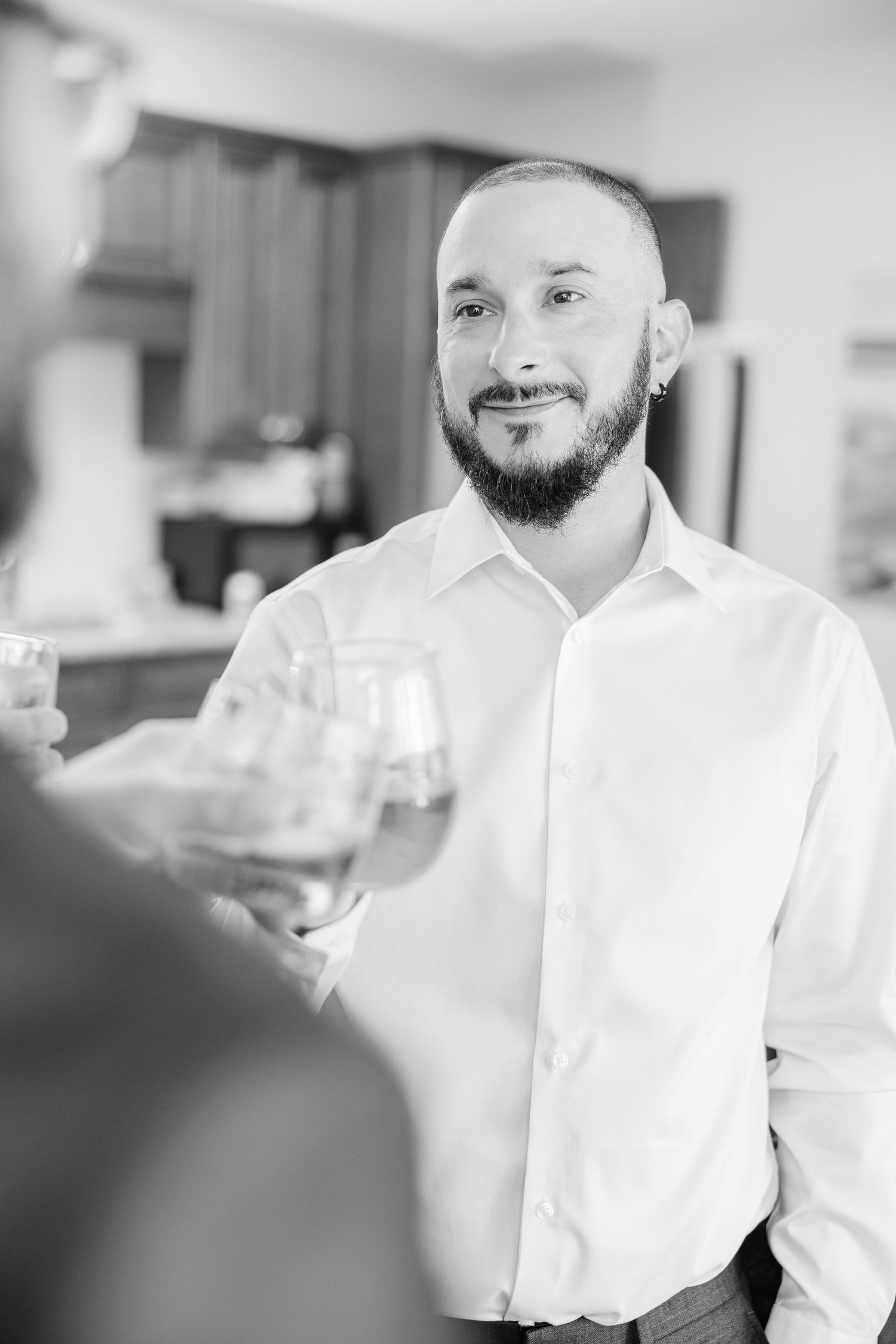 A groom in a white dress shirt smiles while holding a glass during a social event wedding groom bride lake Gaston photographer light airy