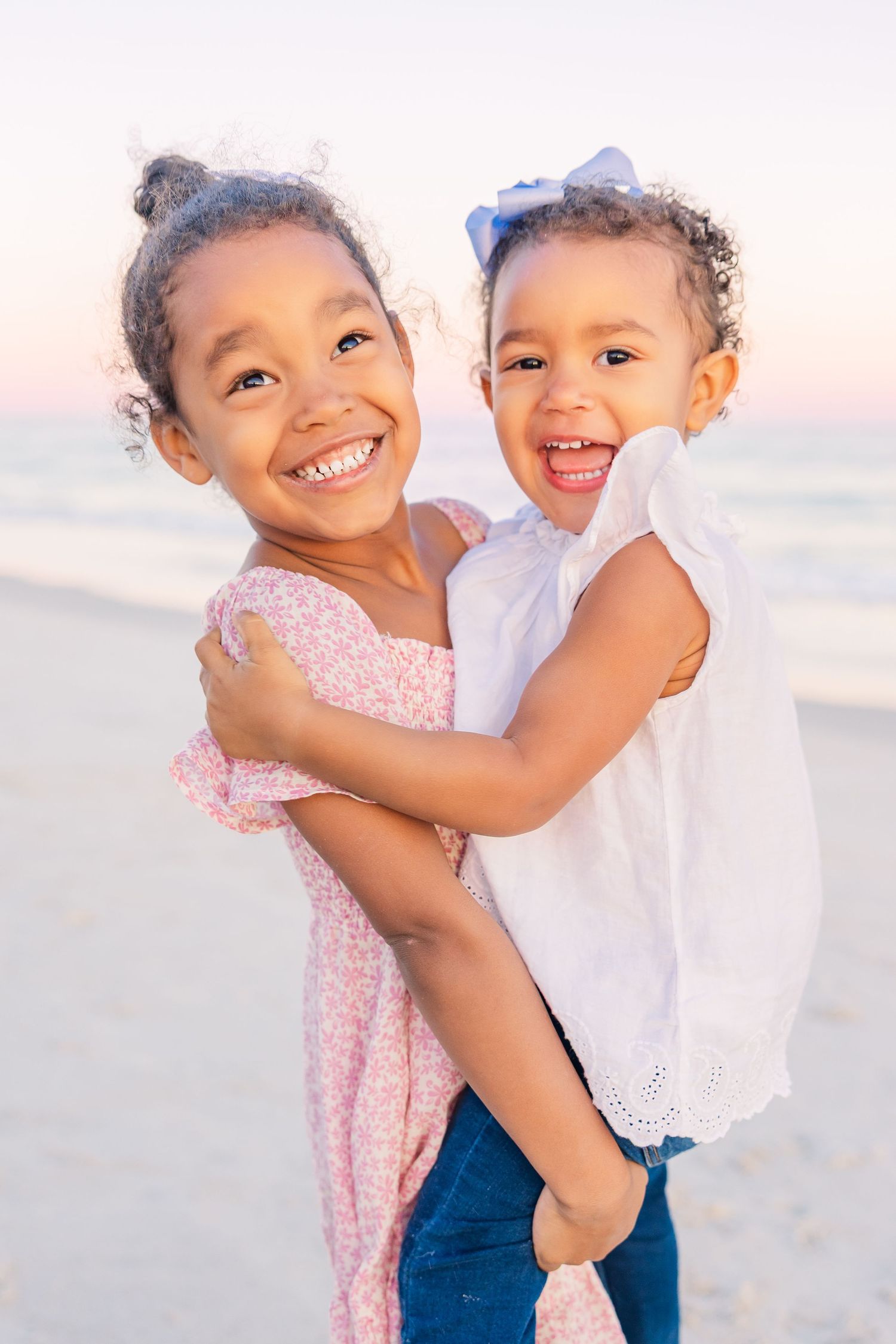 Siblings sharing joyful laughter and embraces during a beach photoshoot at dusk.