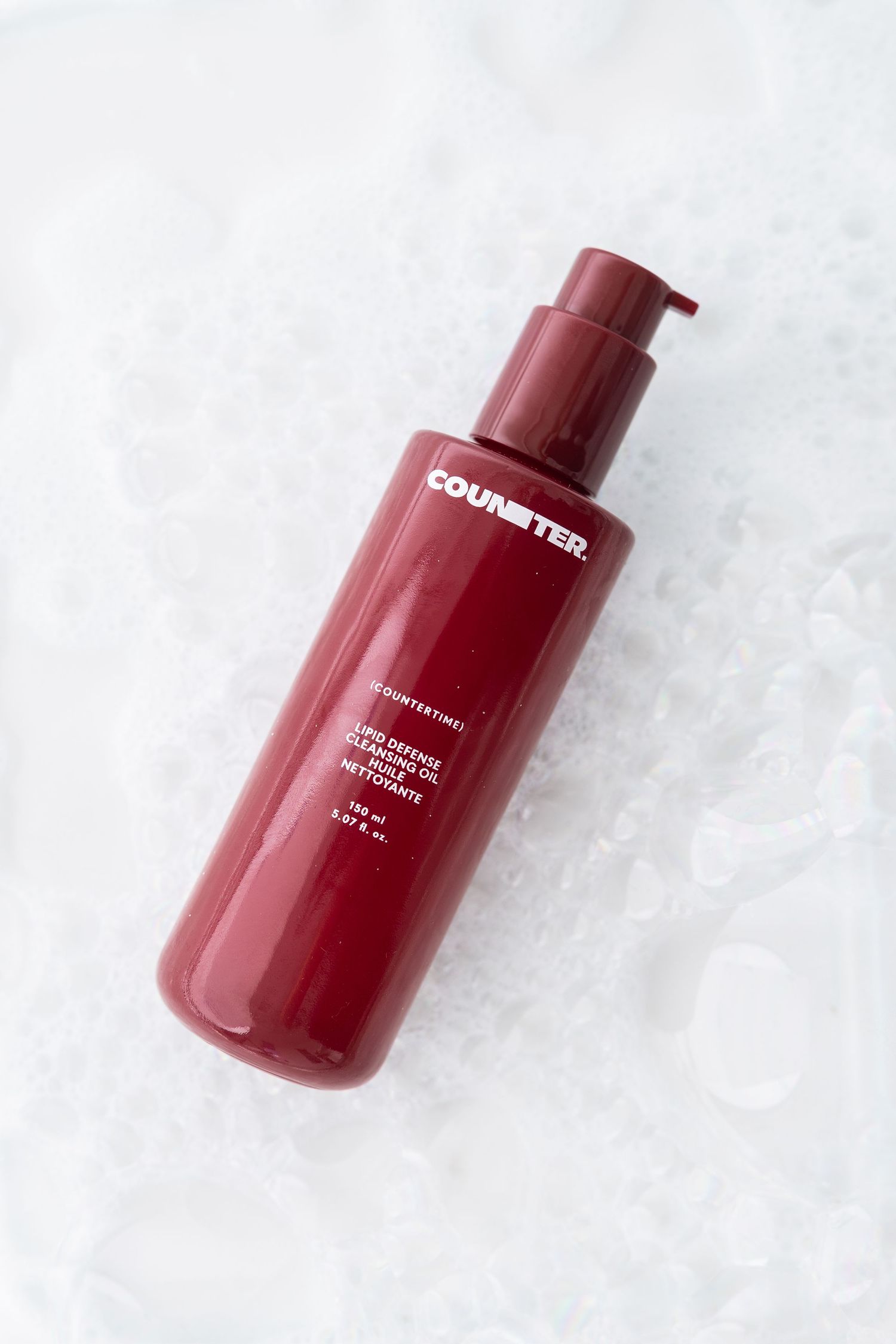 Red cosmetic pump bottle photographed on white textured background.