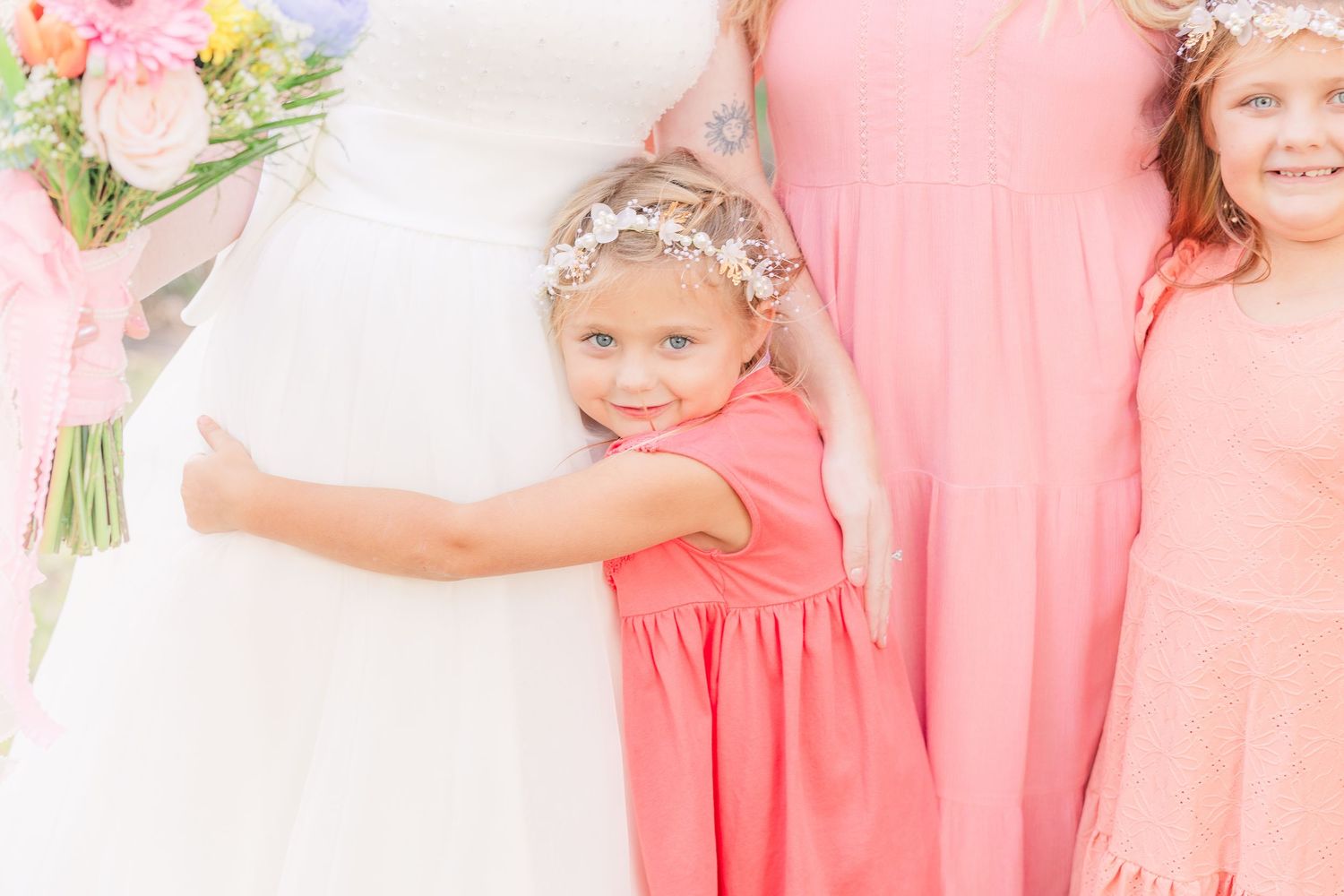 Young bridesmaids in matching coral dresses pose with bright smiles at a spring wedding light and airy wilmington nc