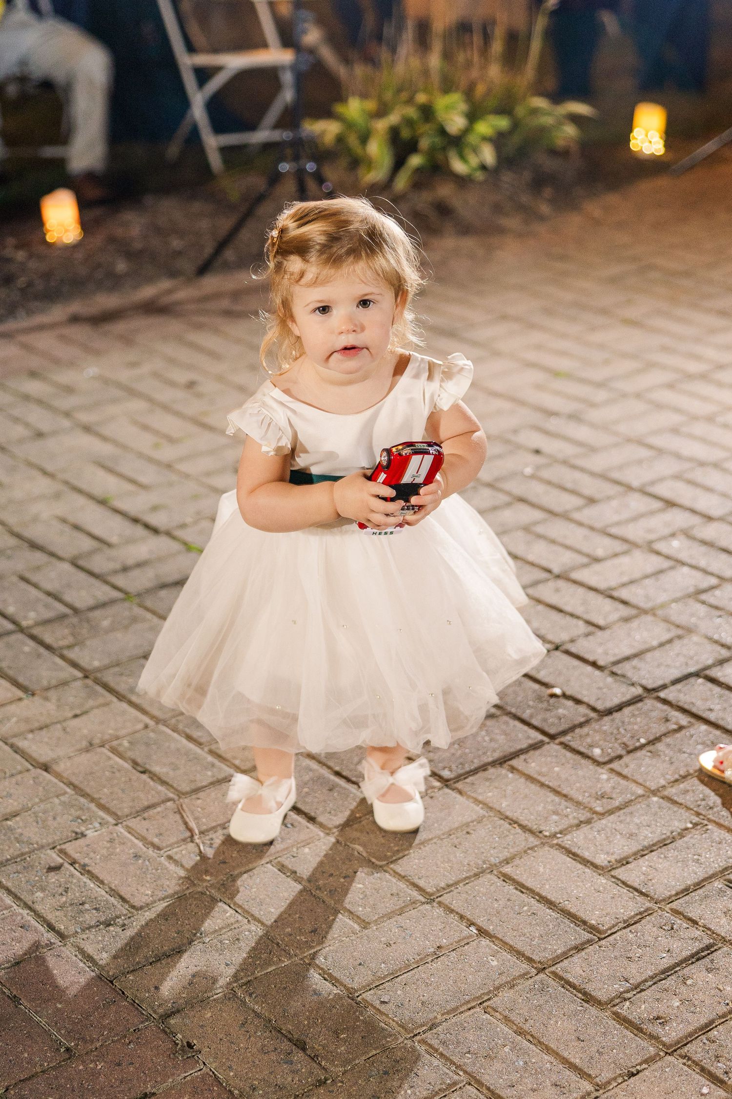 Toddler in white tulle dress playing on stone patio during evening event wedding groom bride lake Gaston photographer light airy