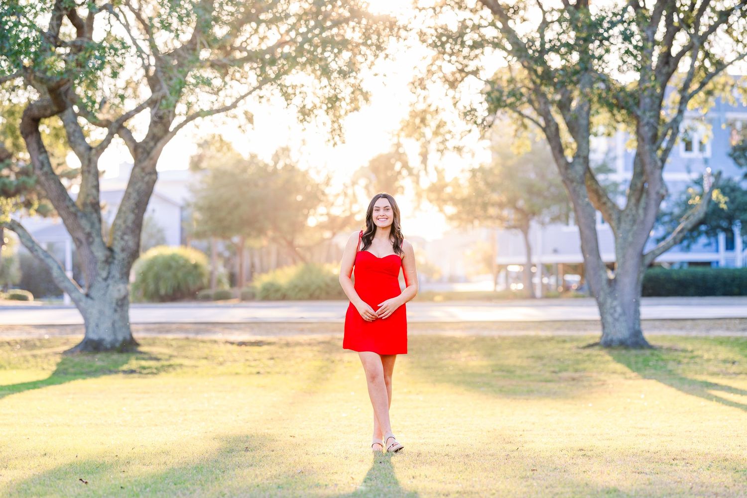 Full length portrait in red dress with sunlit trees in background.