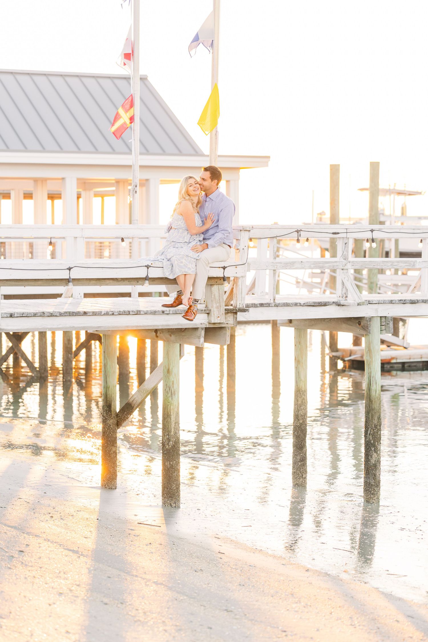 Romantic coastal photo session with couple sitting on dock at sunset.