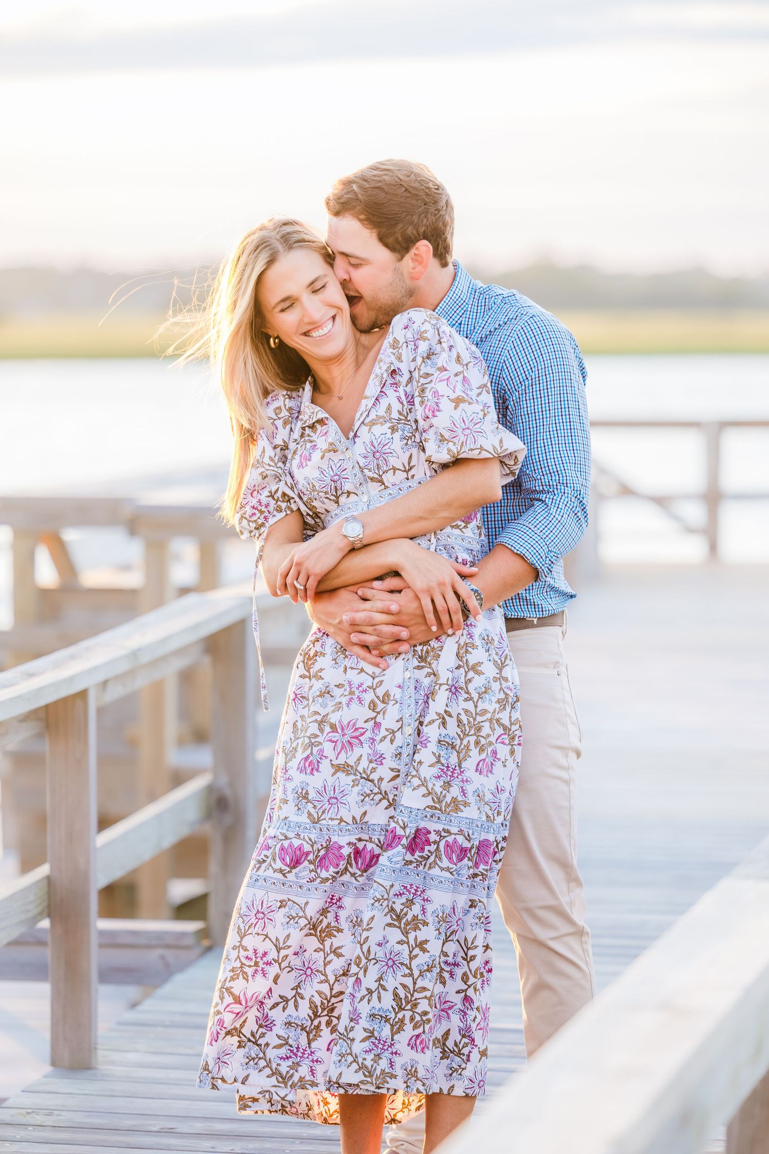 Couple in coordinated blue and floral outfits embracing on a coastal boardwalk at sunset.