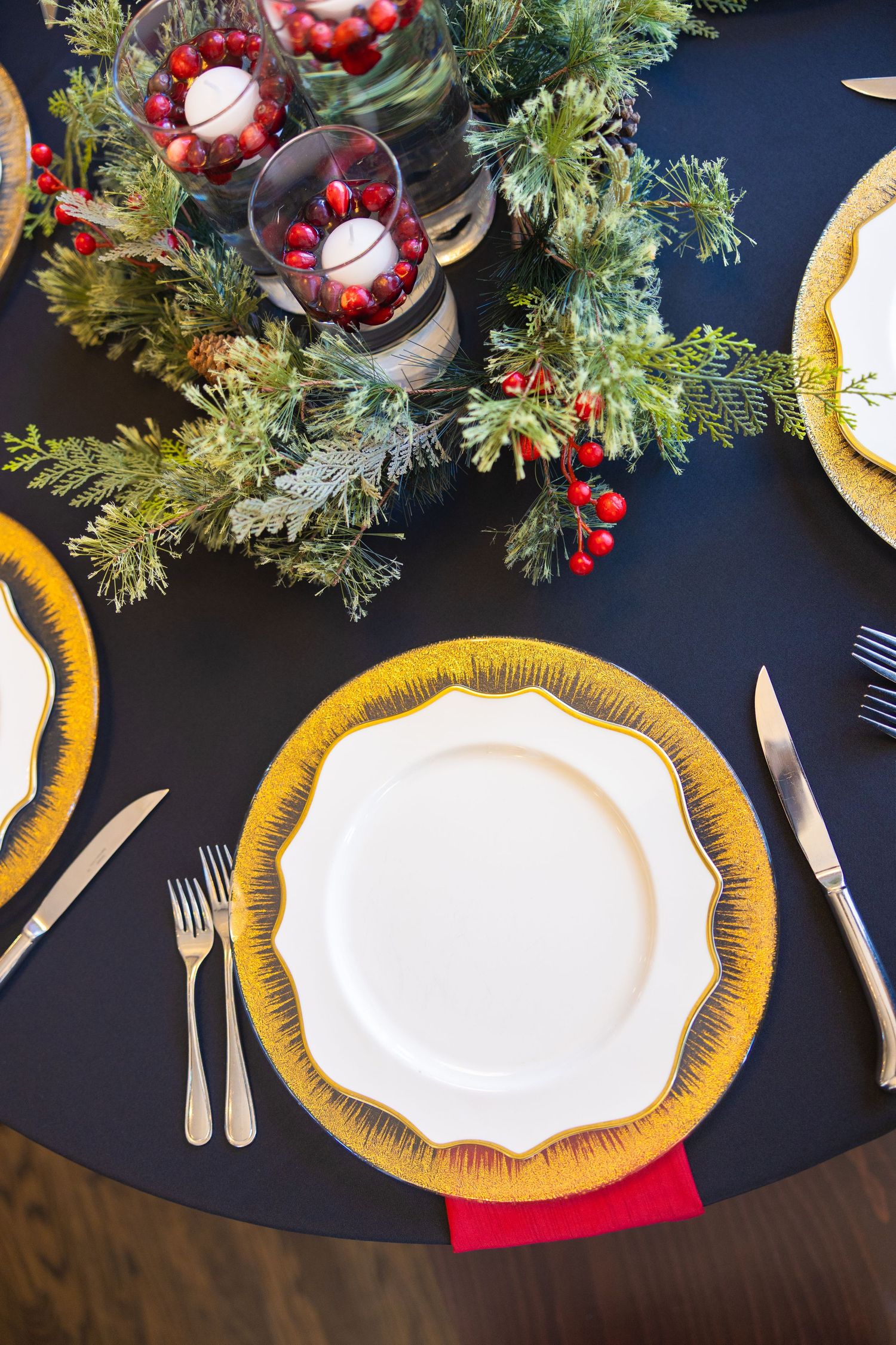 Elegant table setting with gold chargers, white plates and holiday greenery on navy tablecloth.