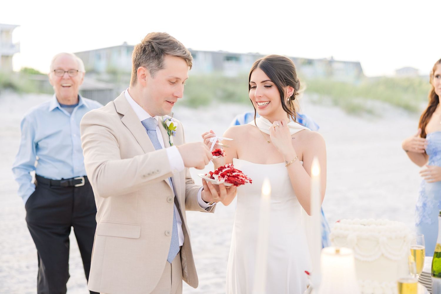 Smiling bride and groom share strawberries during their intimate beach wedding celebration with guests in Carolina Beach near Wilmington, NC