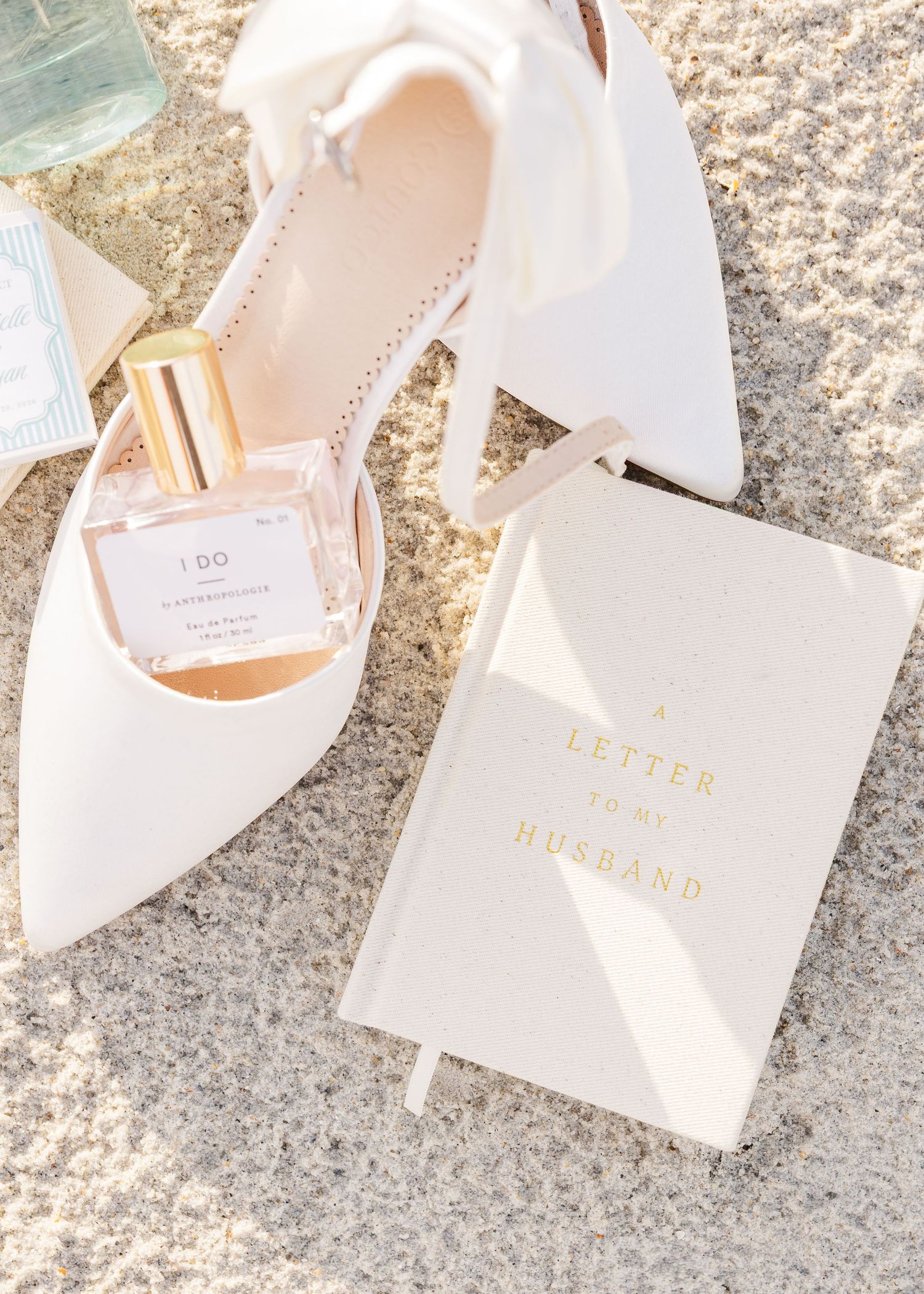 White bridal heels, I Do perfume bottle, and a Letter to My Husband journal arranged on a marble surface.
