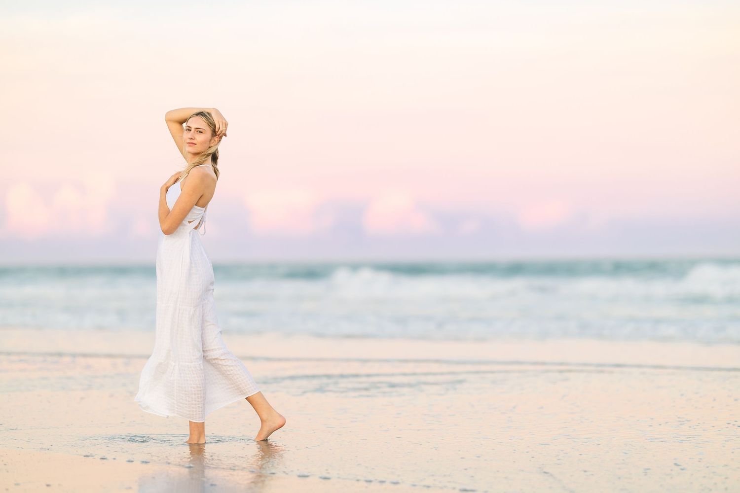 Candid movement shot of woman in white dress on beach at dusk.