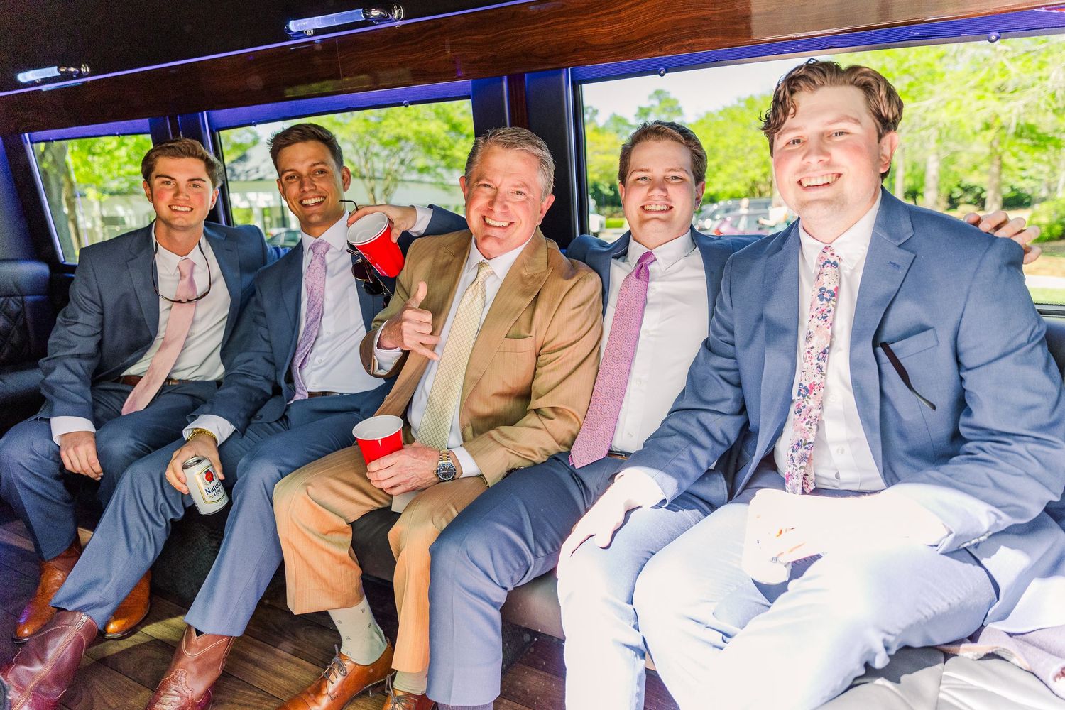 Five men in suits and ties sit together inside a party bus or limousine.