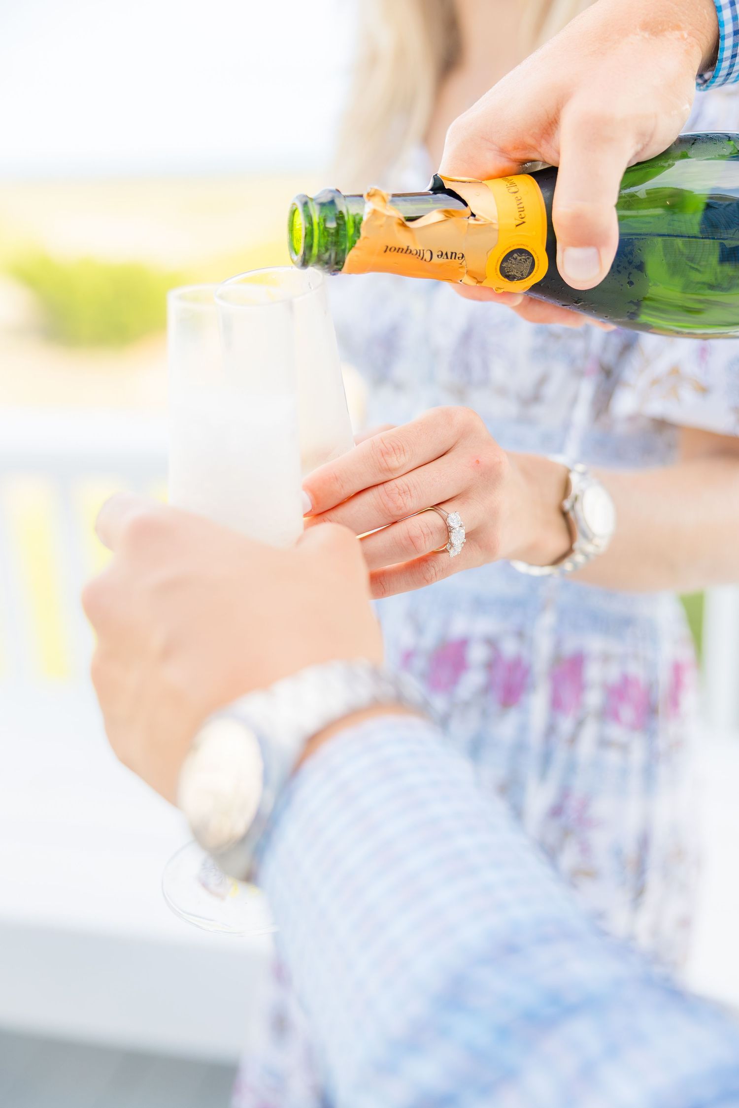 Hands pour champagne into glasses during a sunny outdoor celebration.