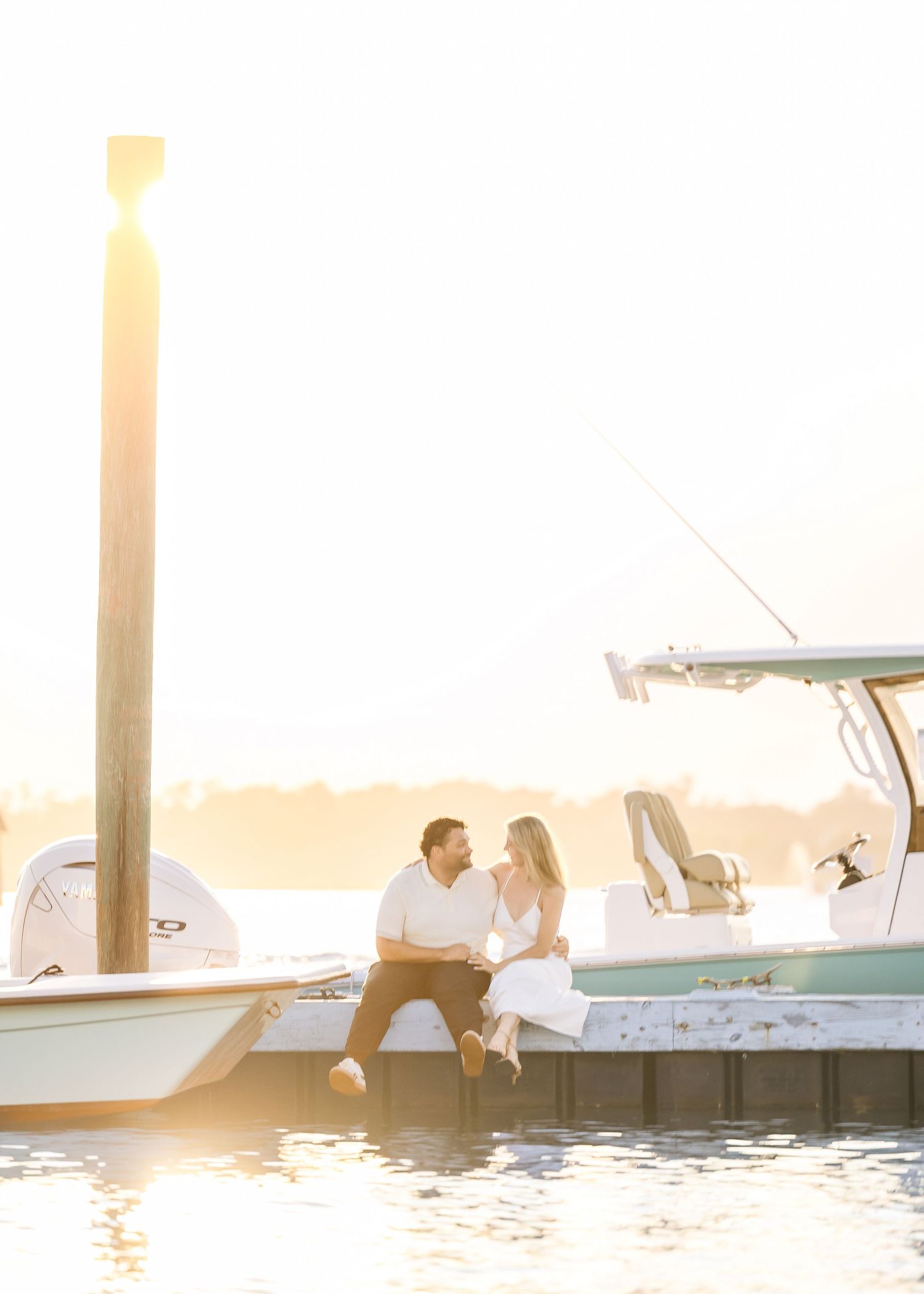Couple sits closely on a boat dock sharing an intimate moment at glowing sunset.