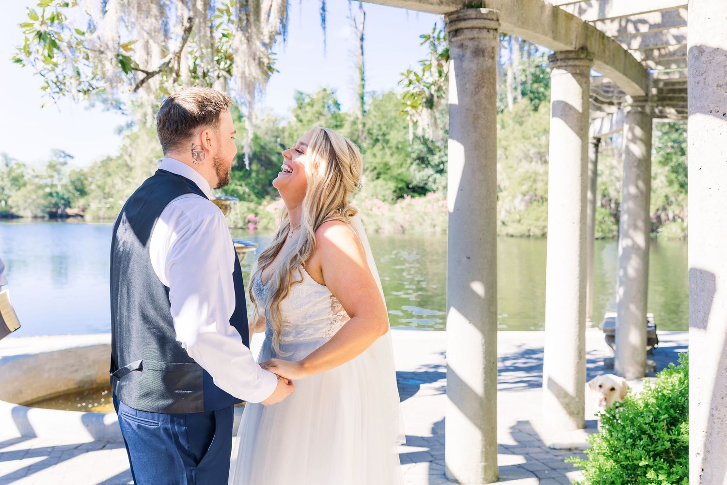 A bride and groom share a romantic moment under a pergola near a serene lake on their wedding day in Airlie Gardens in Wilmington, NC