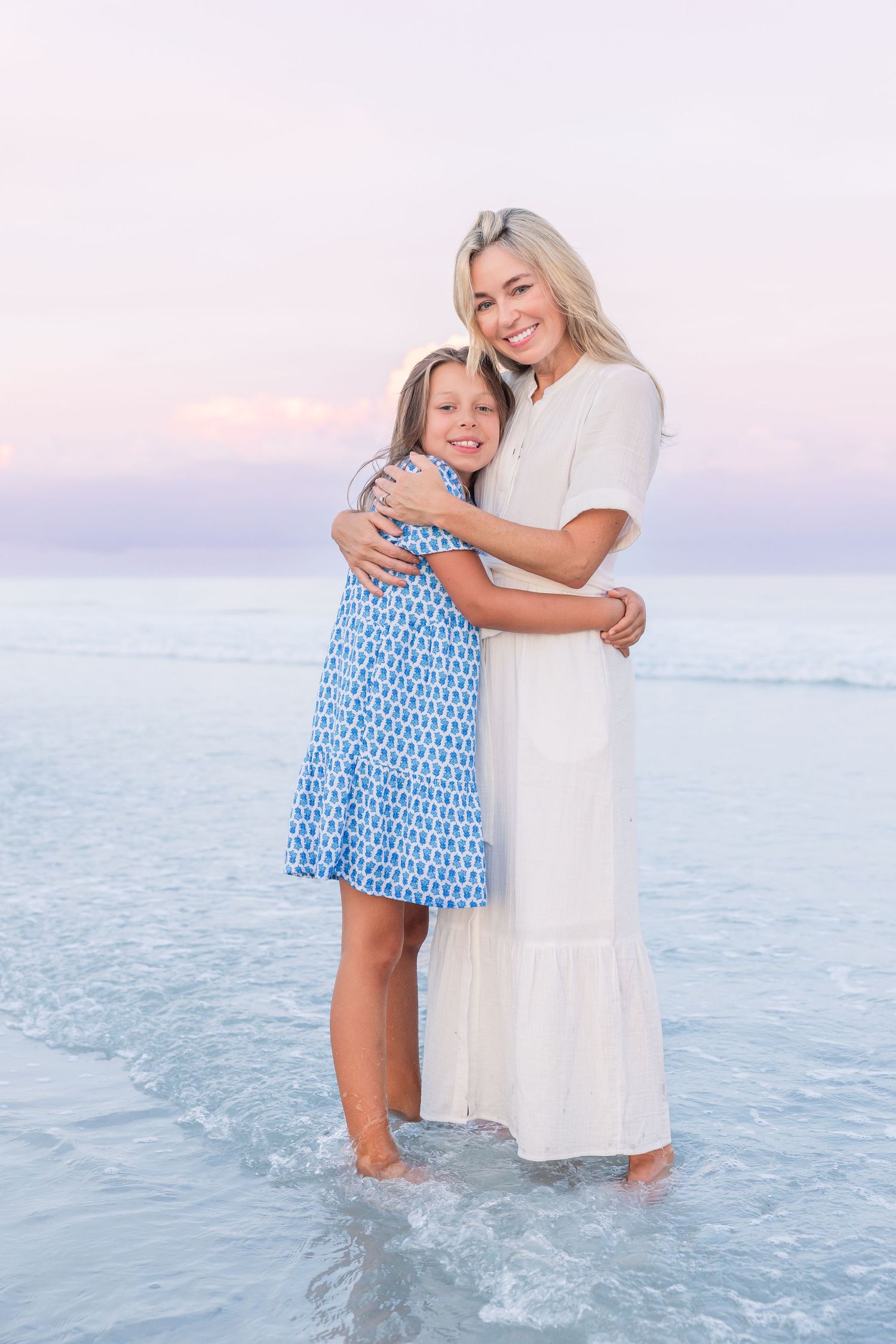 A sweet moment between family members standing in the ocean waves at sunset.