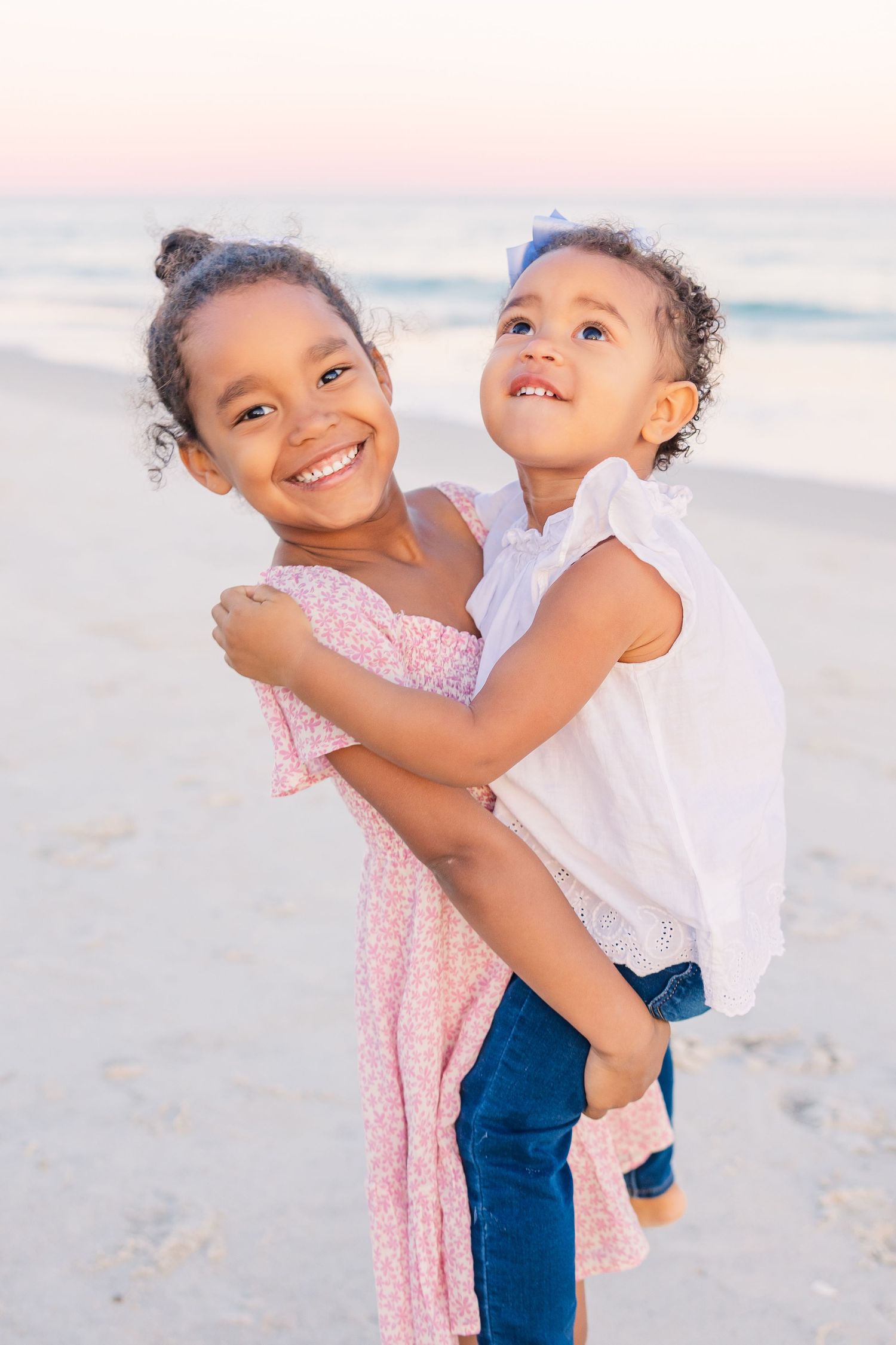 Two children hugging and playing together on a sandy beach at sunset.