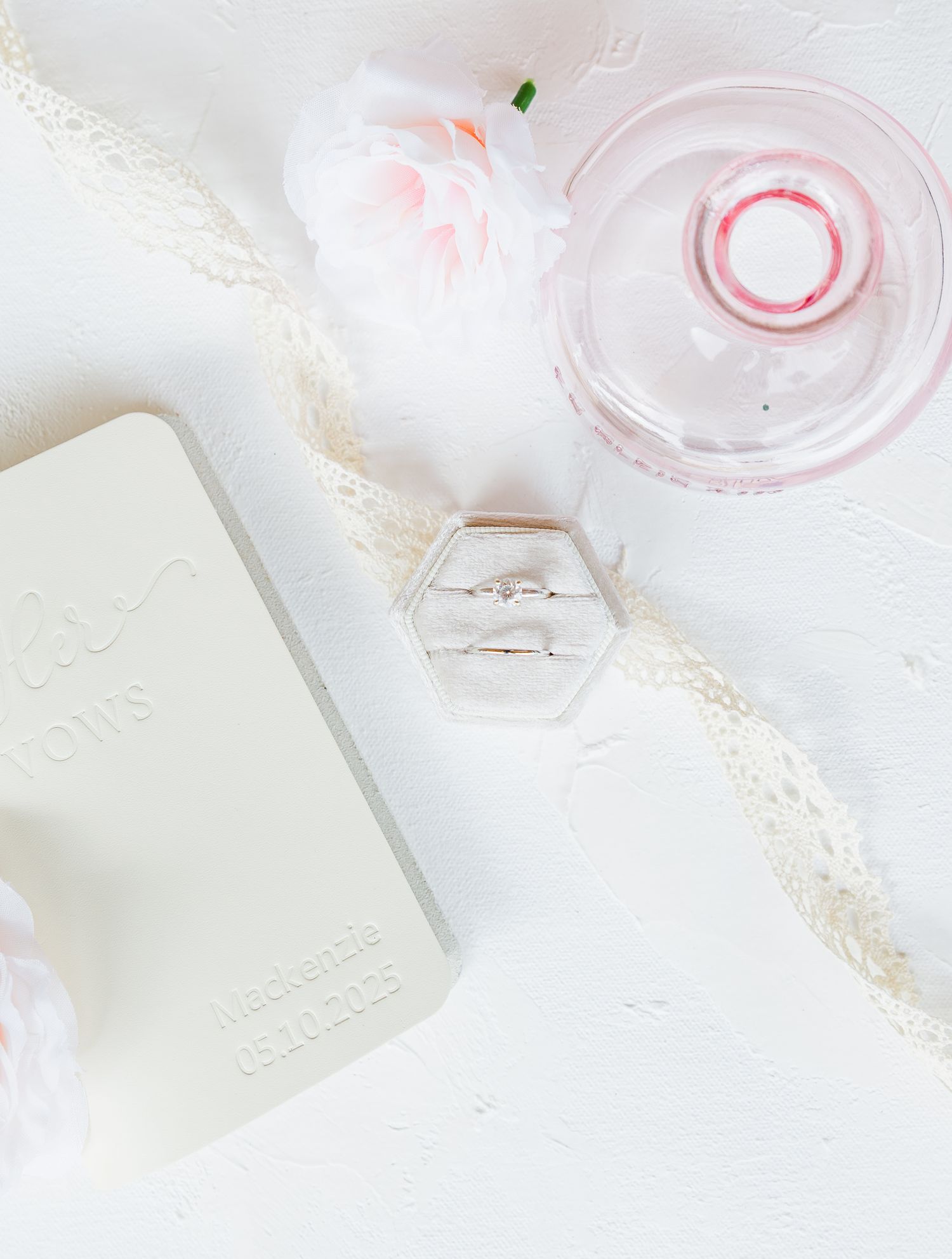 Delicate white wedding details including a lace trim, ring box, and pink floral accents on a light background light and airy wedding