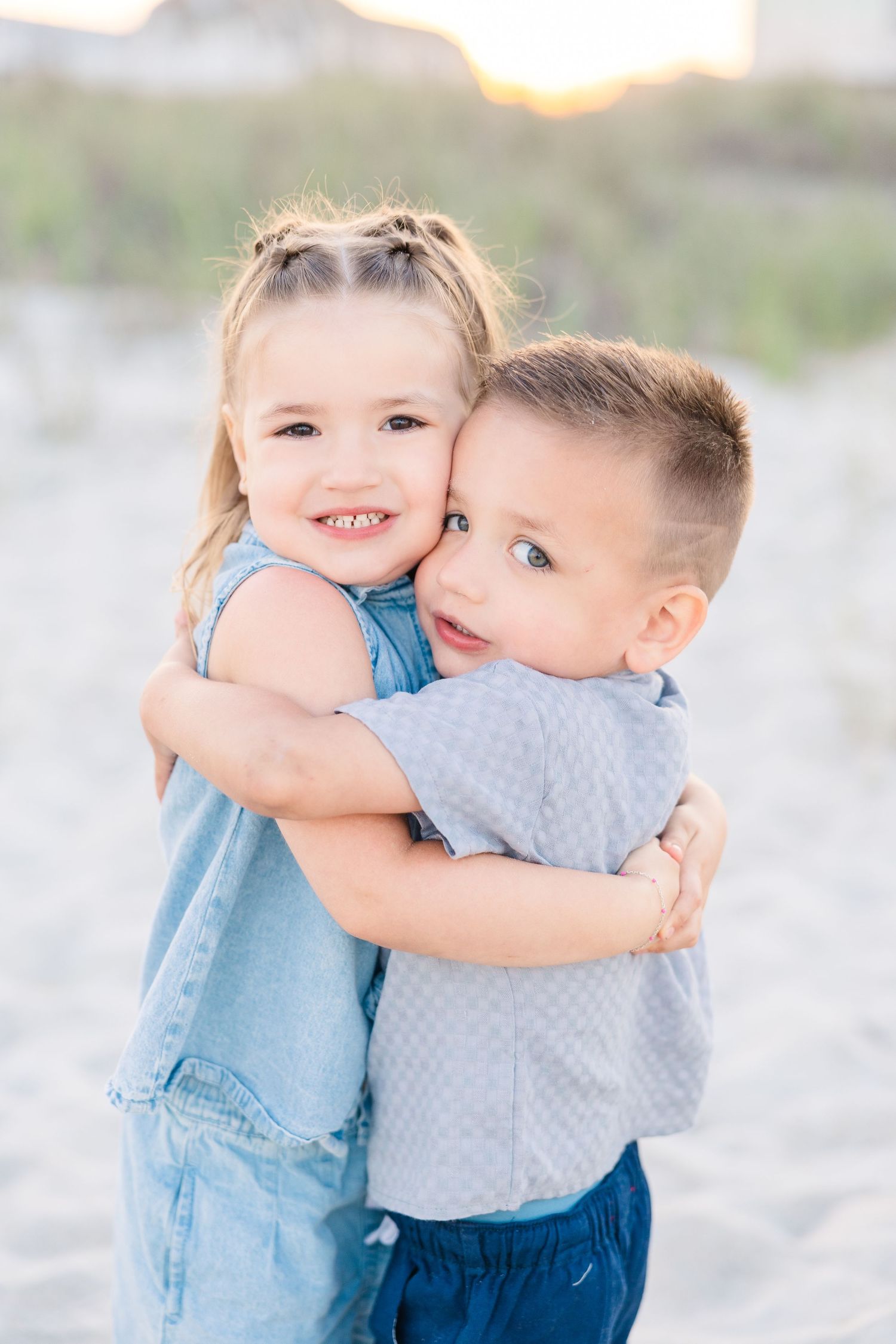 Two young children hugging and smiling on a sandy beach at sunset.