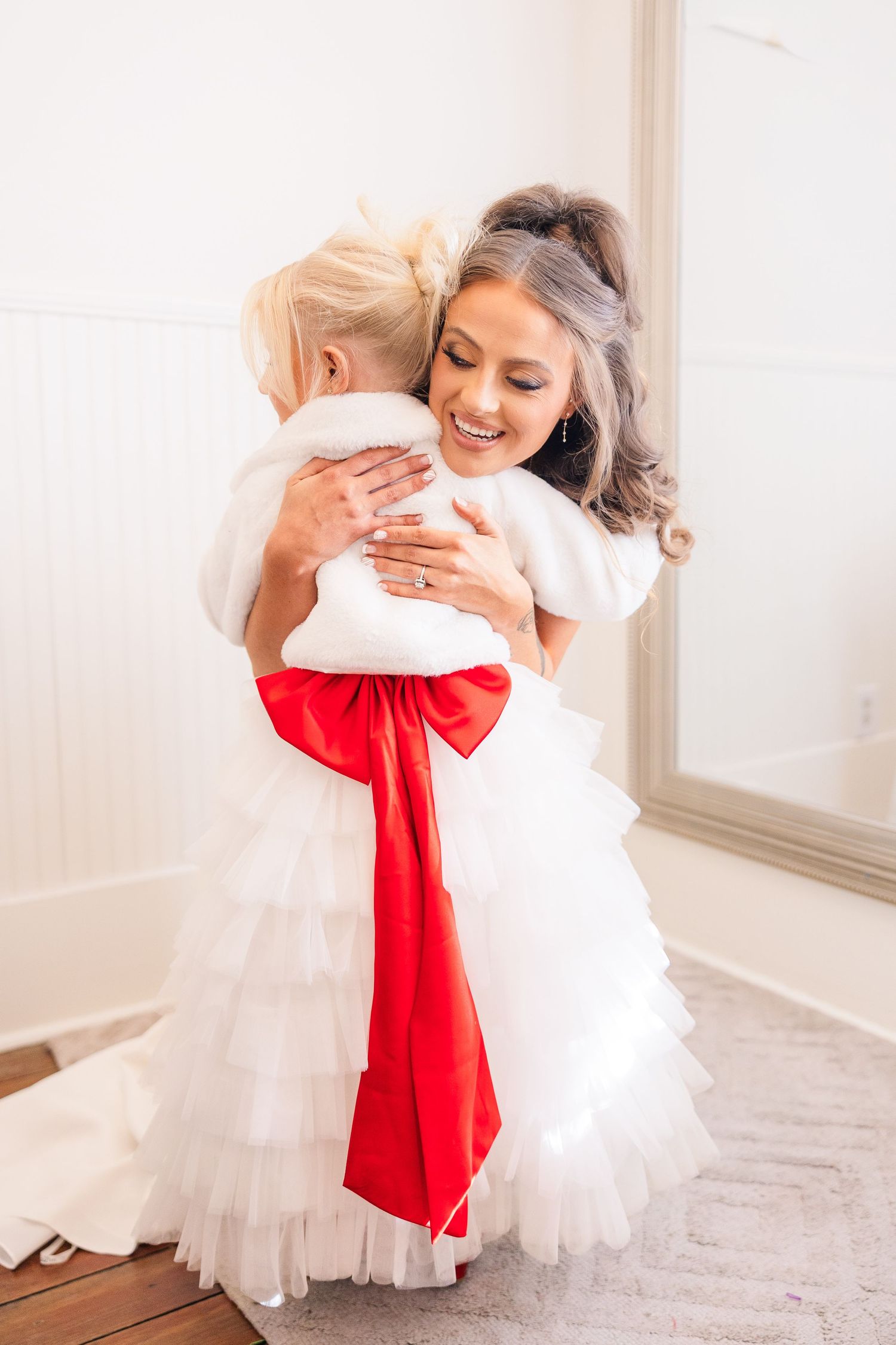 Sweet moment during wedding preparations with white dress and red bow accent.