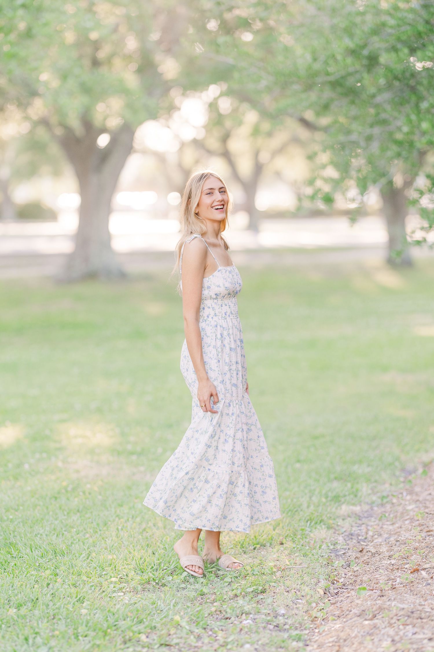 Light and airy outdoor portrait in a white floral dress among garden trees.