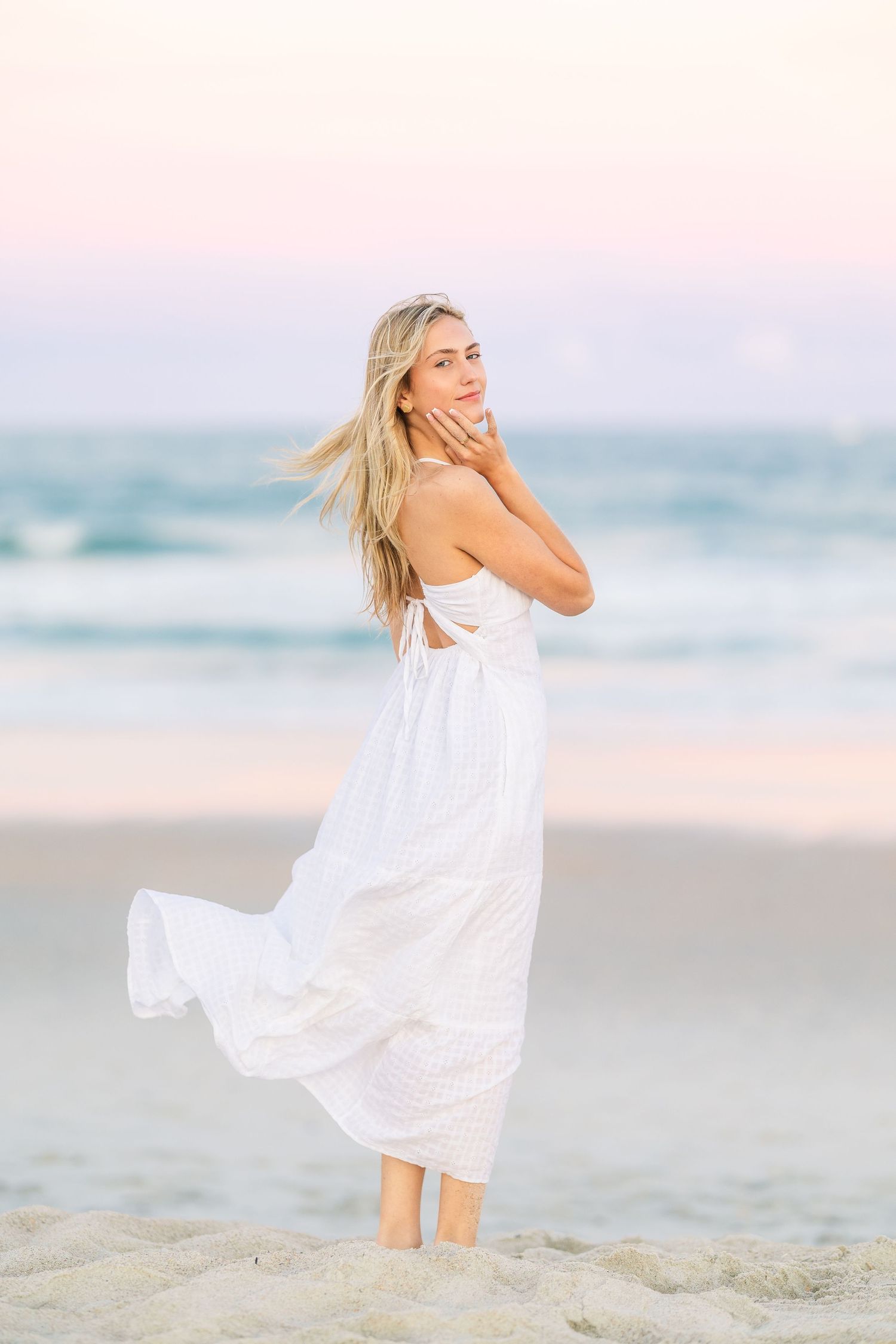 A person in a white maxi dress twirls on the beach with hair flowing in the ocean breeze.