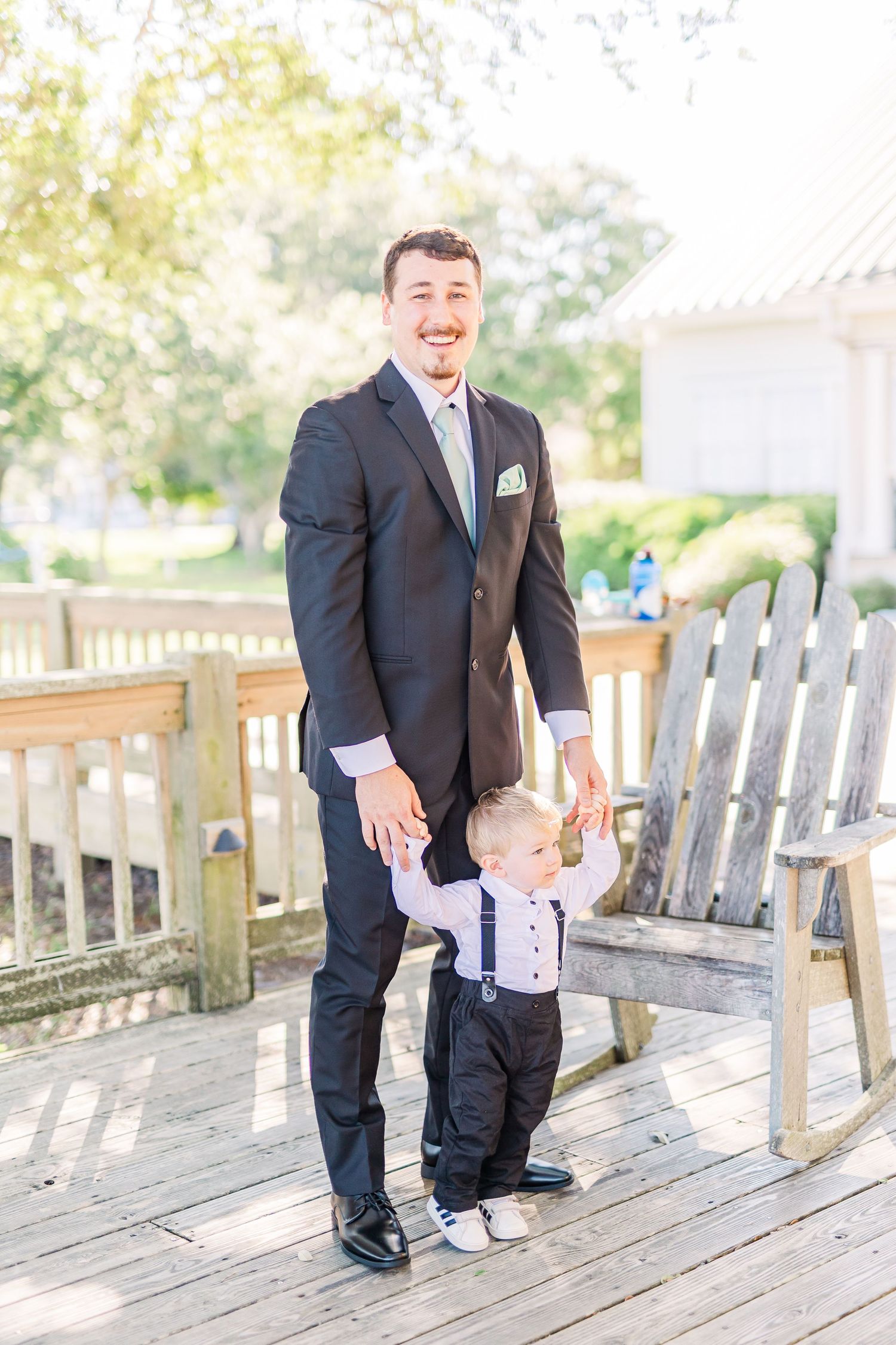 Father and son in matching suits share sweet moment on wooden deck southport elopement wedding bride groom light and airy classic