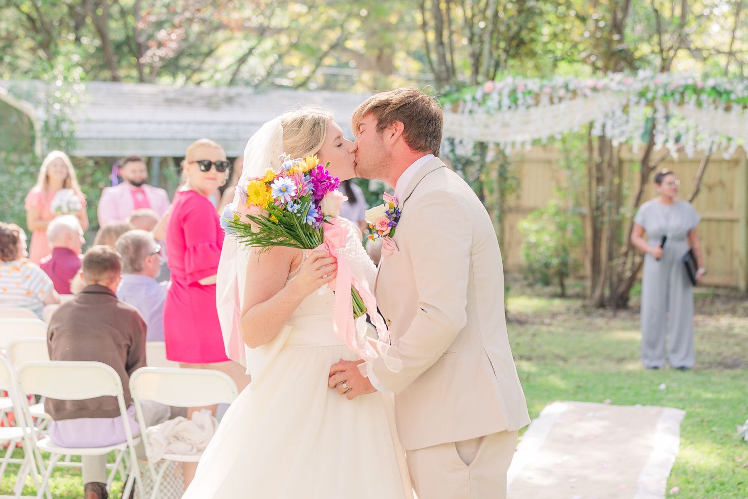Sunny outdoor wedding celebration with guests in bright colors and natural garden backdrop wedding groom bride wilmington photographer light