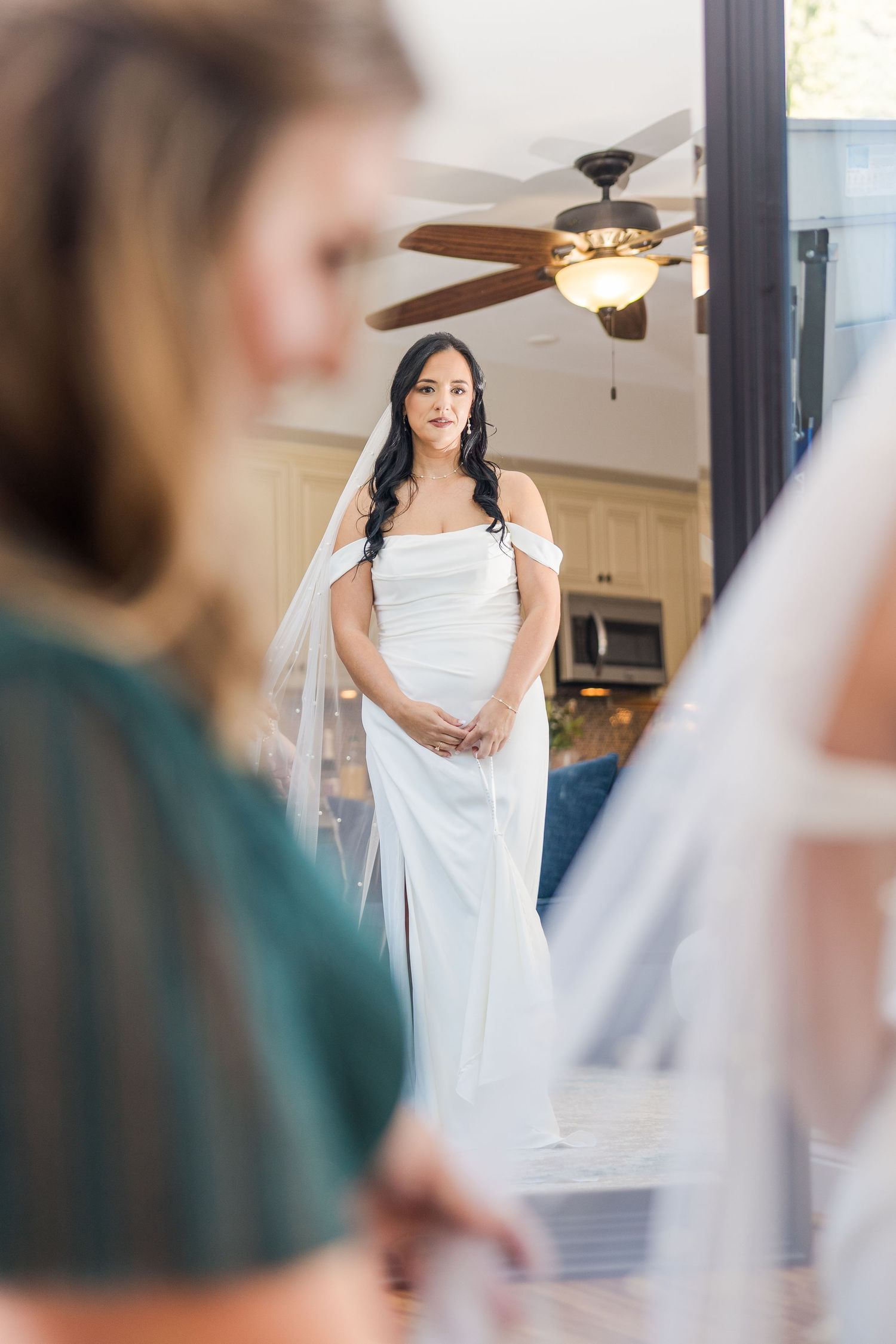 Bride in off-shoulder dress stands elegantly in front of mirror during wedding preparations wedding groom bride lake Gaston photographer lig