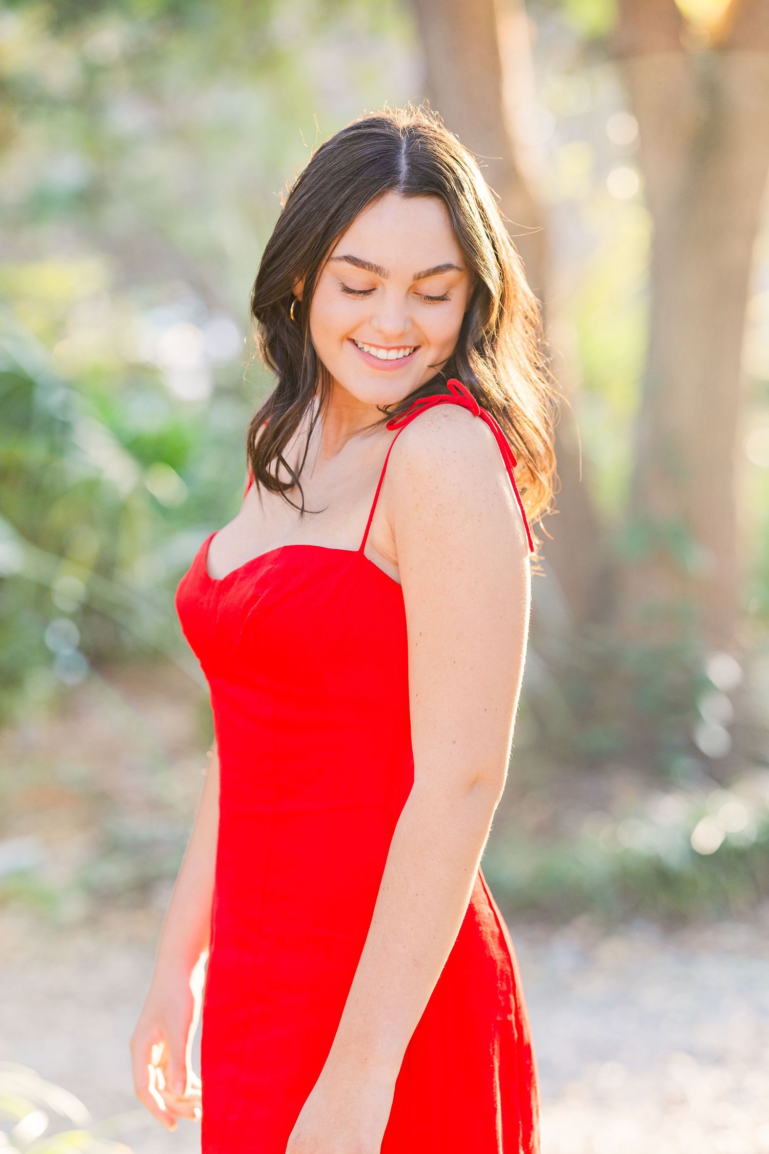Sun-dappled portrait session featuring a vibrant red dress in a garden setting.