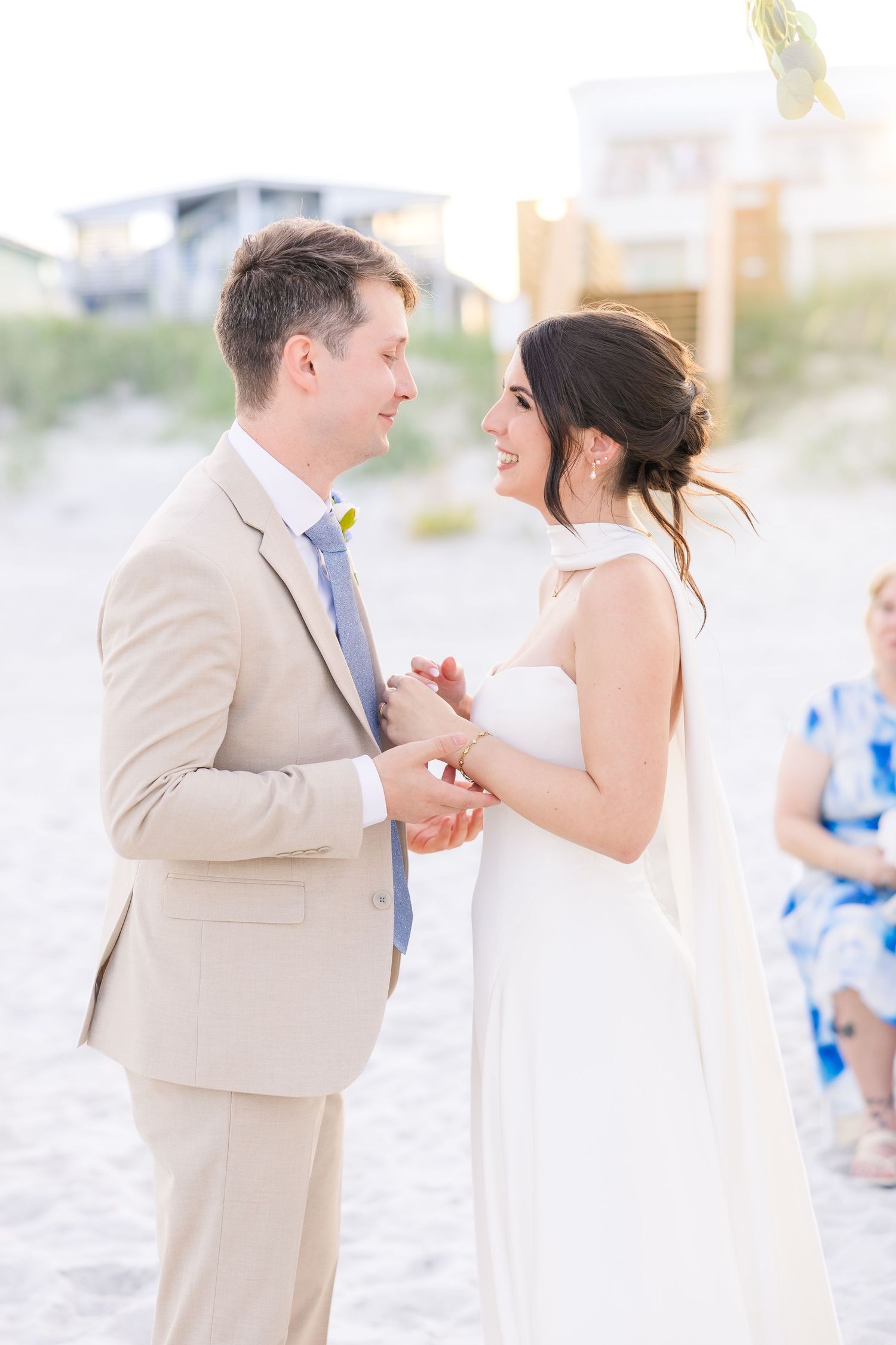 Groom in tan suit placing ring on brides finger during outdoor beach wedding ceremony in Carolina Beach near Wilmington, NC.