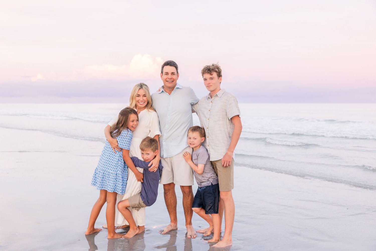 A family enjoys a beach photoshoot together wearing coordinated outfits in soft evening light.