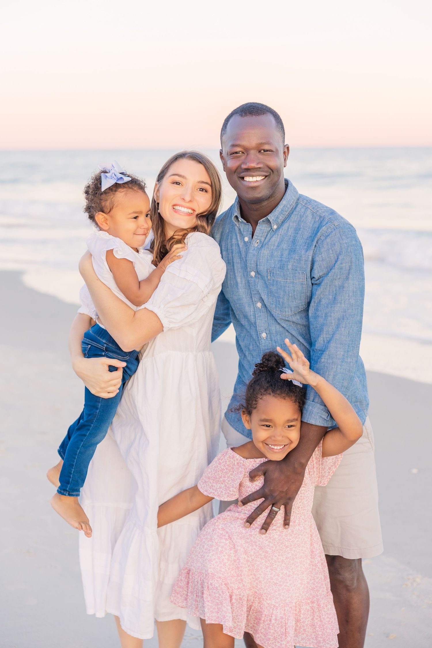 Happy family enjoying a sunset photoshoot together on the beach in coordinated blue and white outfits.