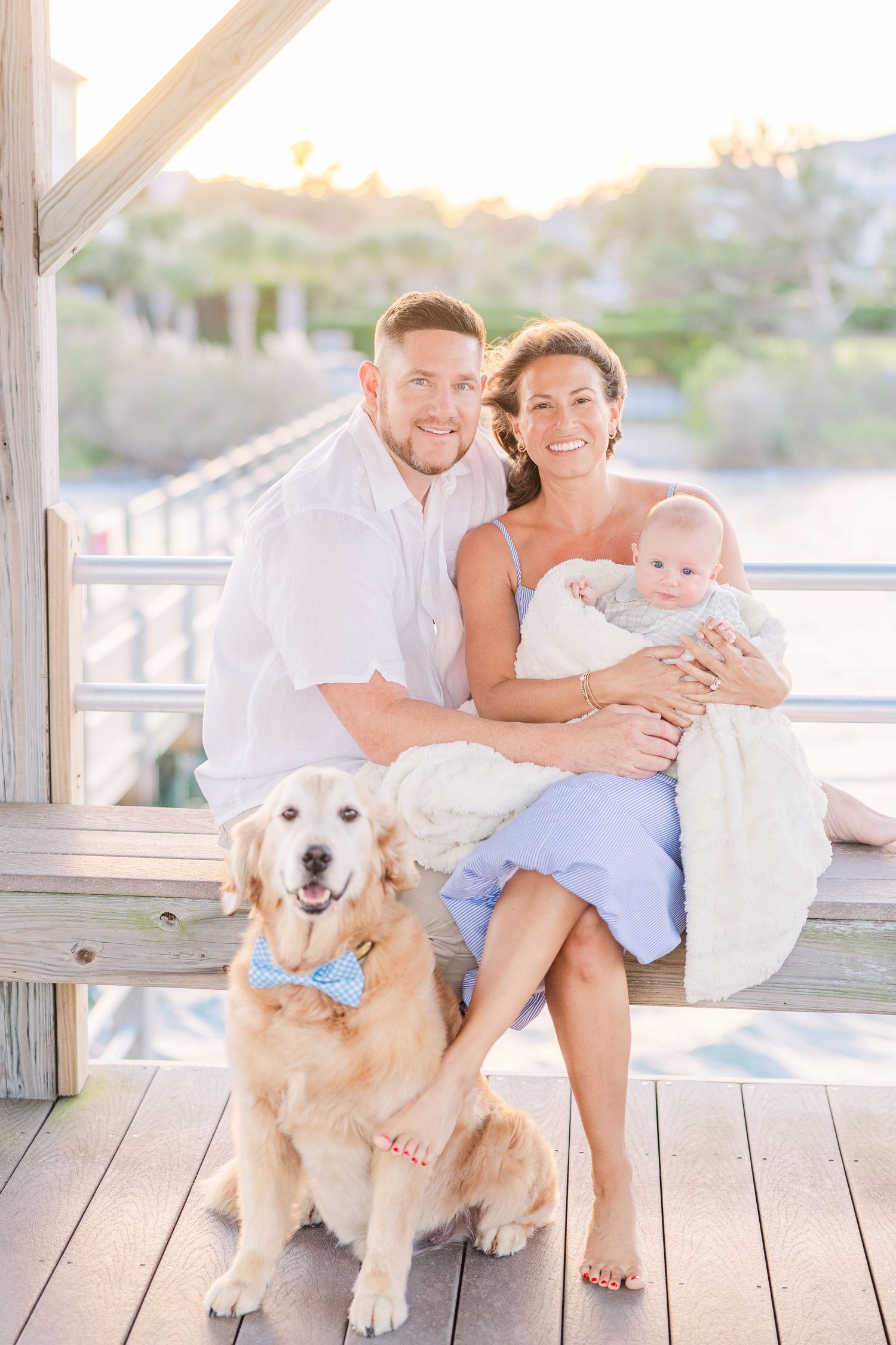 Family sits on wooden deck with golden retriever dog during sunset photo session.