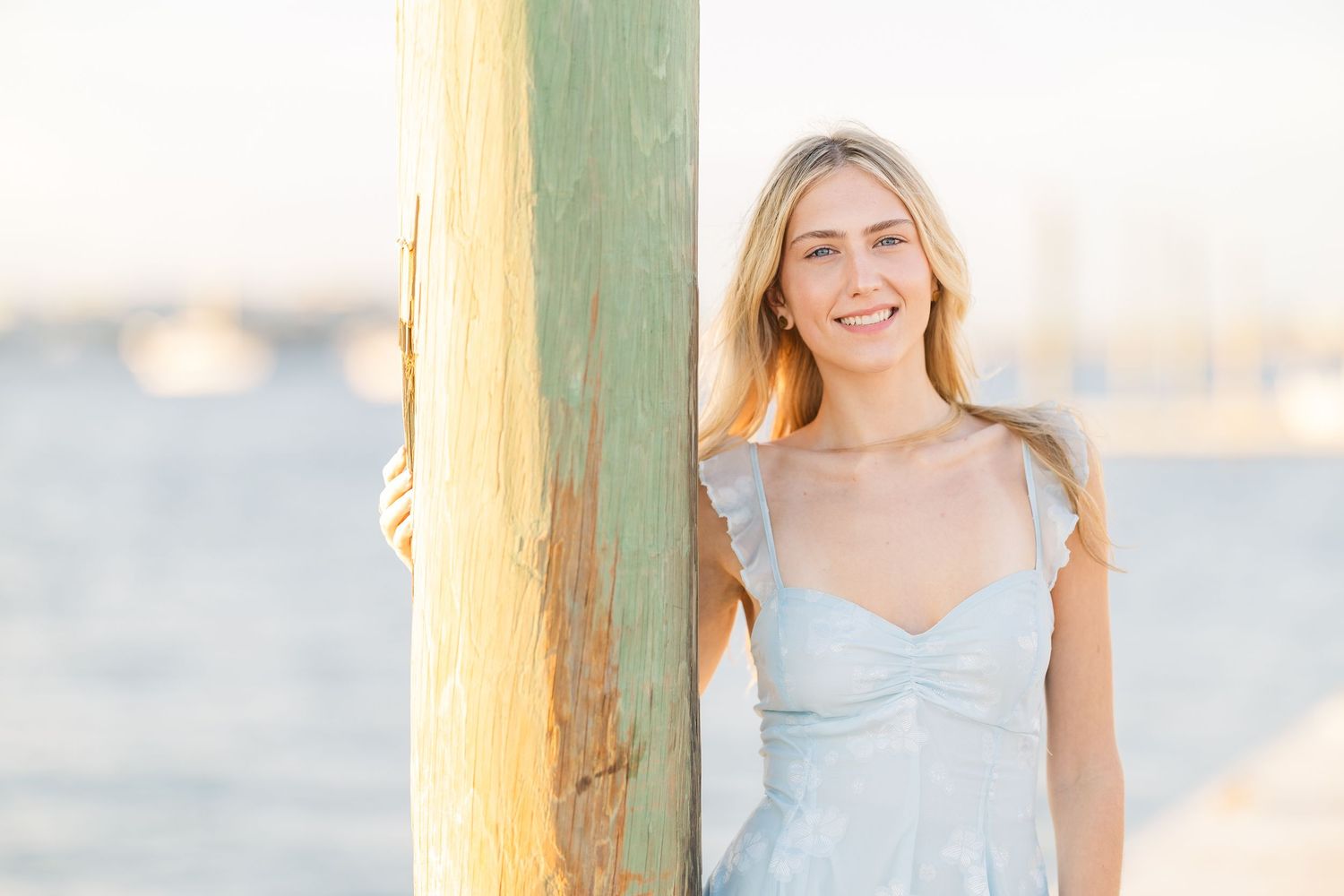 Casual beachside portrait against yellow post in pale blue summer dress.