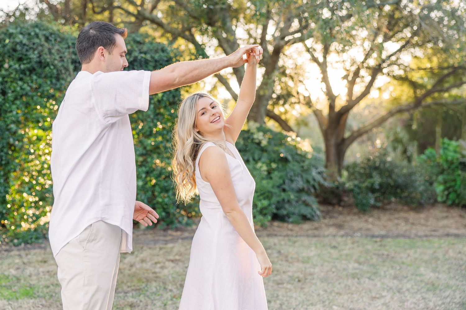 A couple shares playful dance moves on a grassy hillside during sunset.