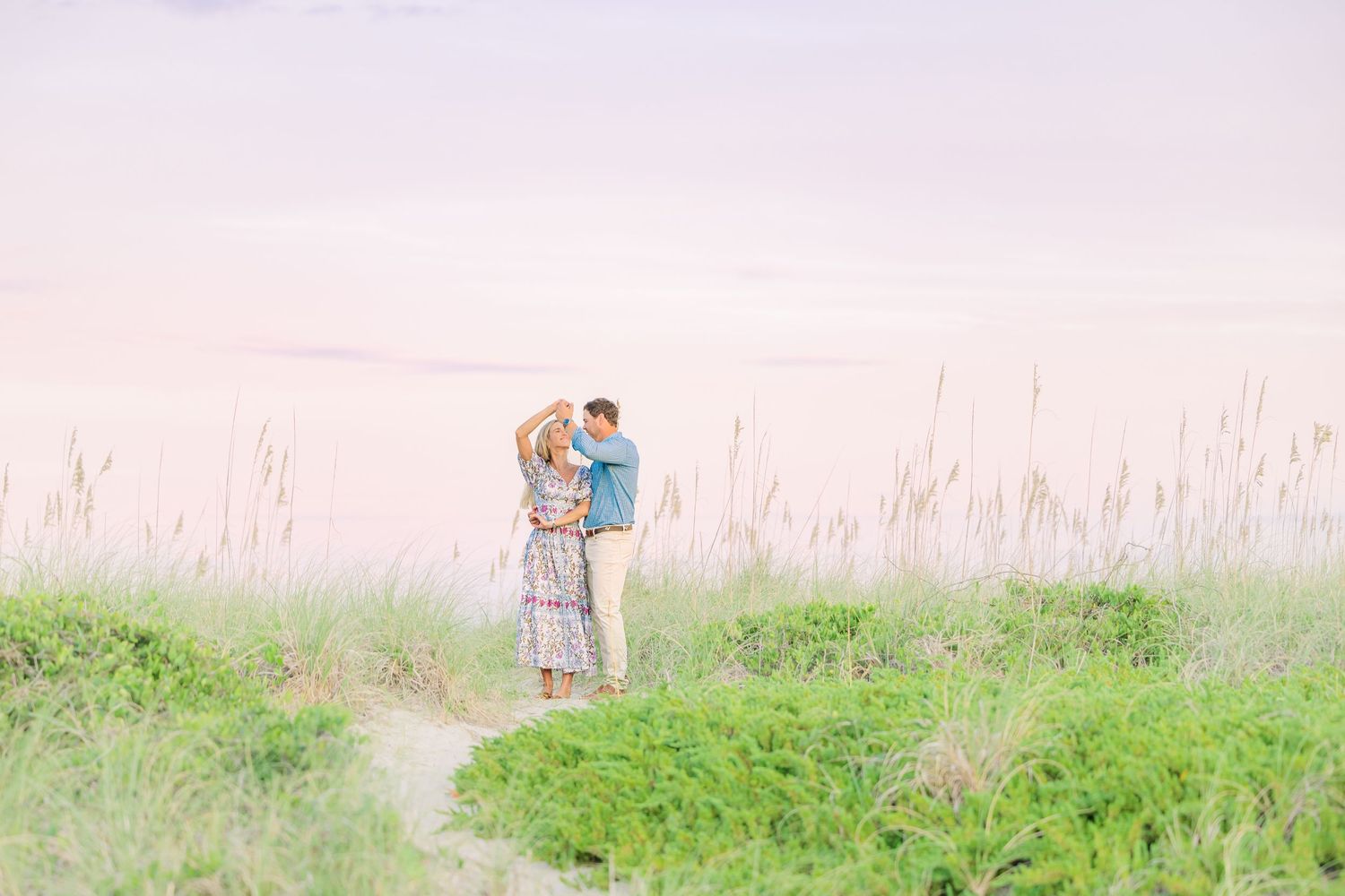 Couple sharing intimate moments in a seaside field during golden hour.