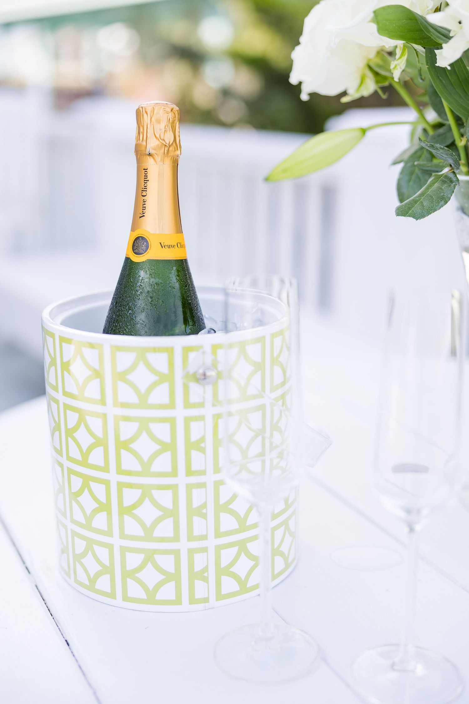 Champagne bottles chilling in decorative geometric pattern ice buckets with white floral arrangements.