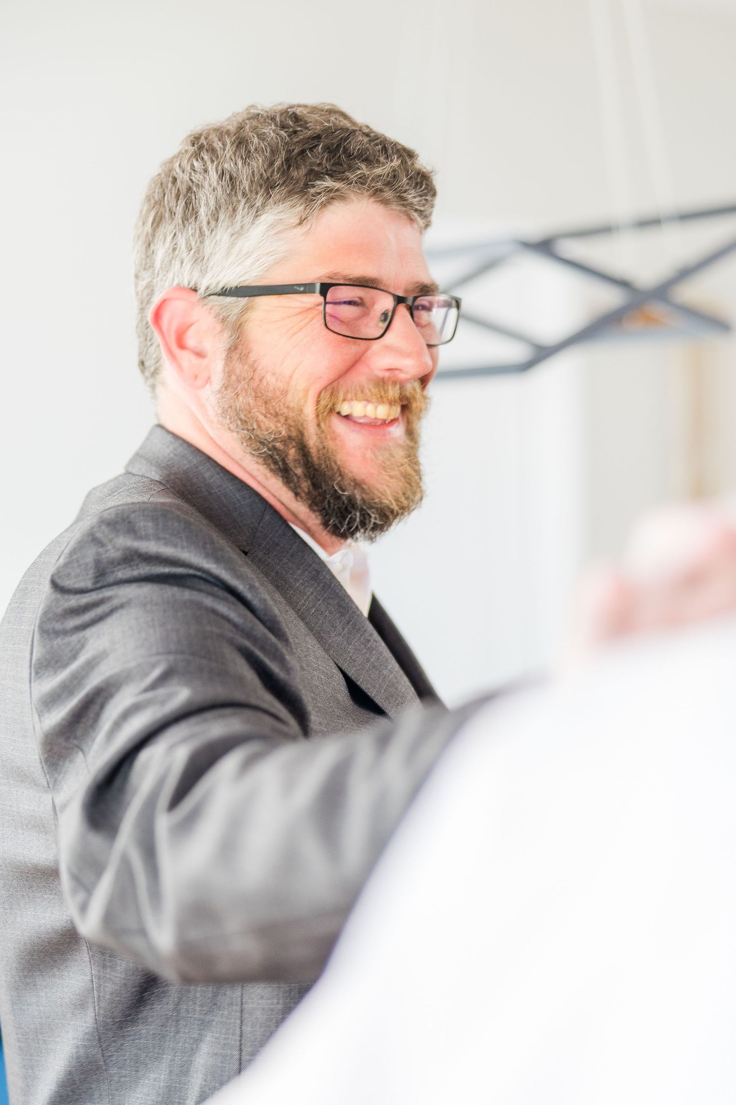 A person in glasses and a suit jacket smiles warmly while holding a glass during a celebration wedding groom bride lake Gaston photographer