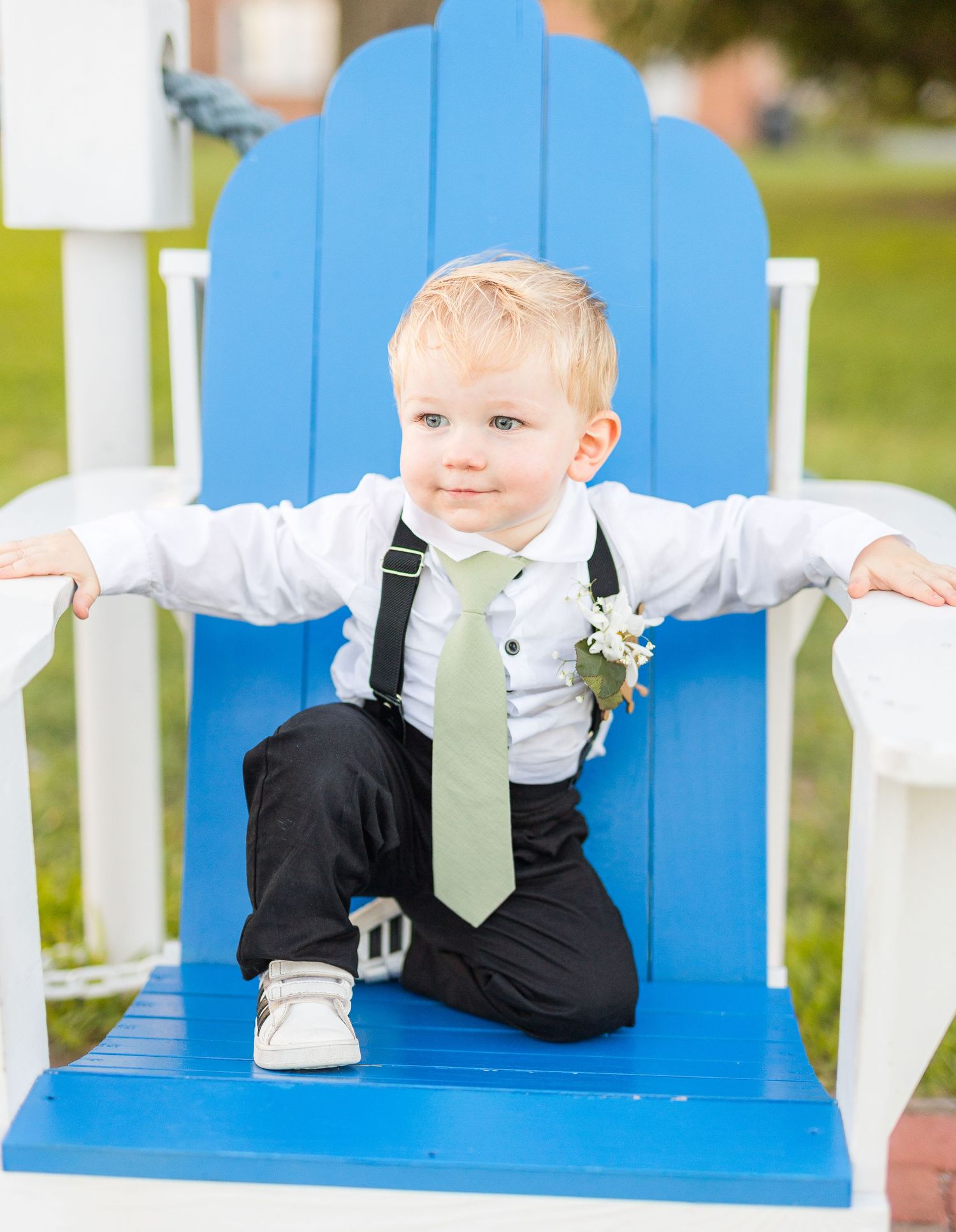 Small child in formal wear poses on bright blue Adirondack chair during wedding celebration southport elopement wedding bride groom light