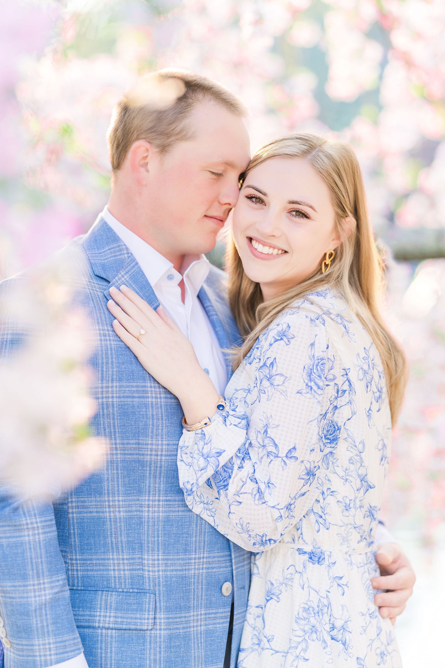 A romantic engagement photo with cherry blossoms featuring coordinating blue and white spring outfits.
