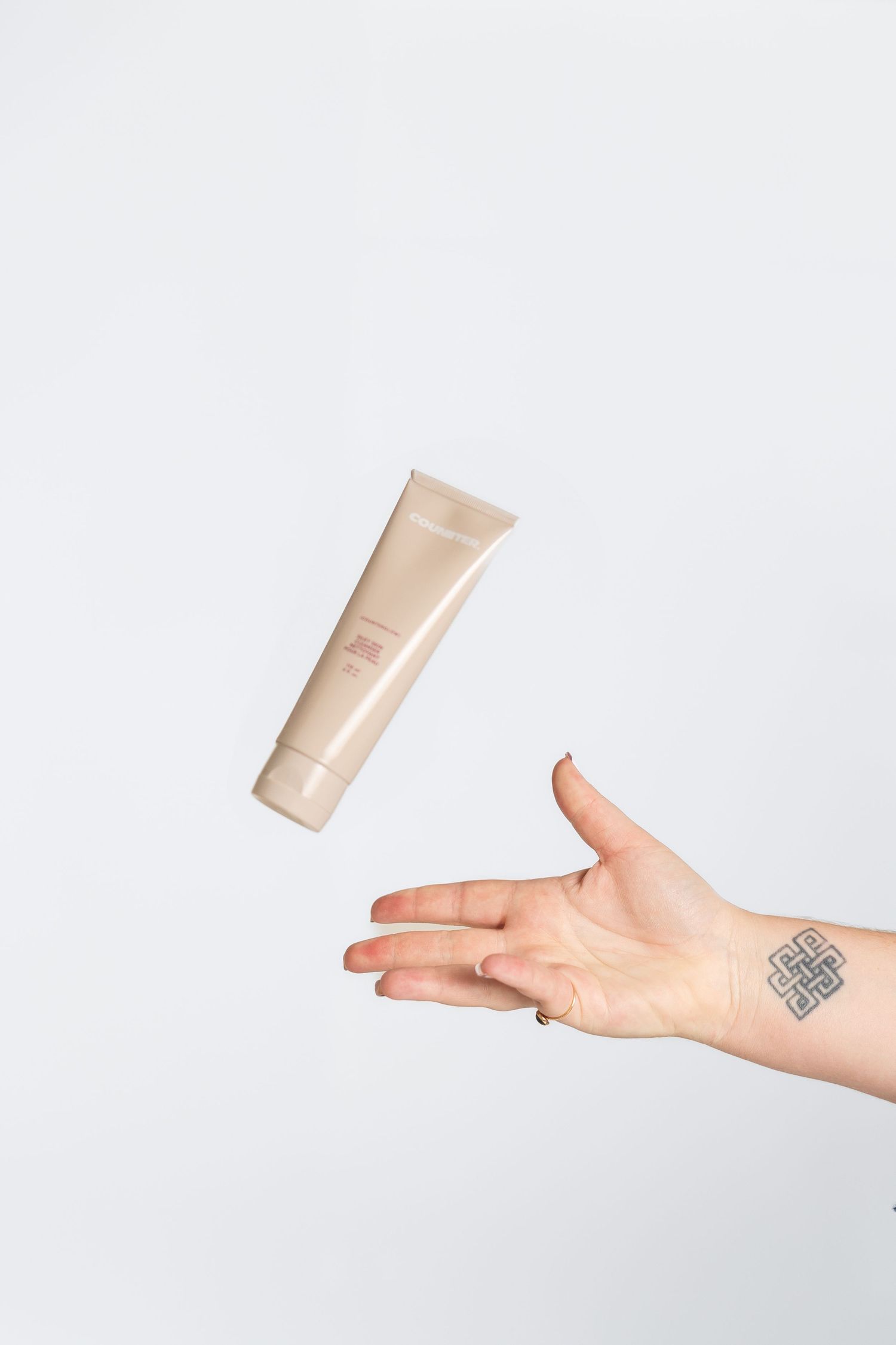 Hand tossing beige cosmetic tube in levitation photography style.