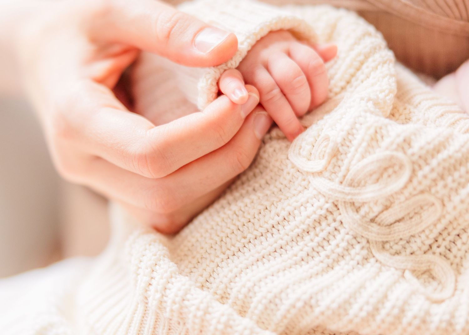 Close up of tiny baby hands and fingers being held gently in soft natural lighting.