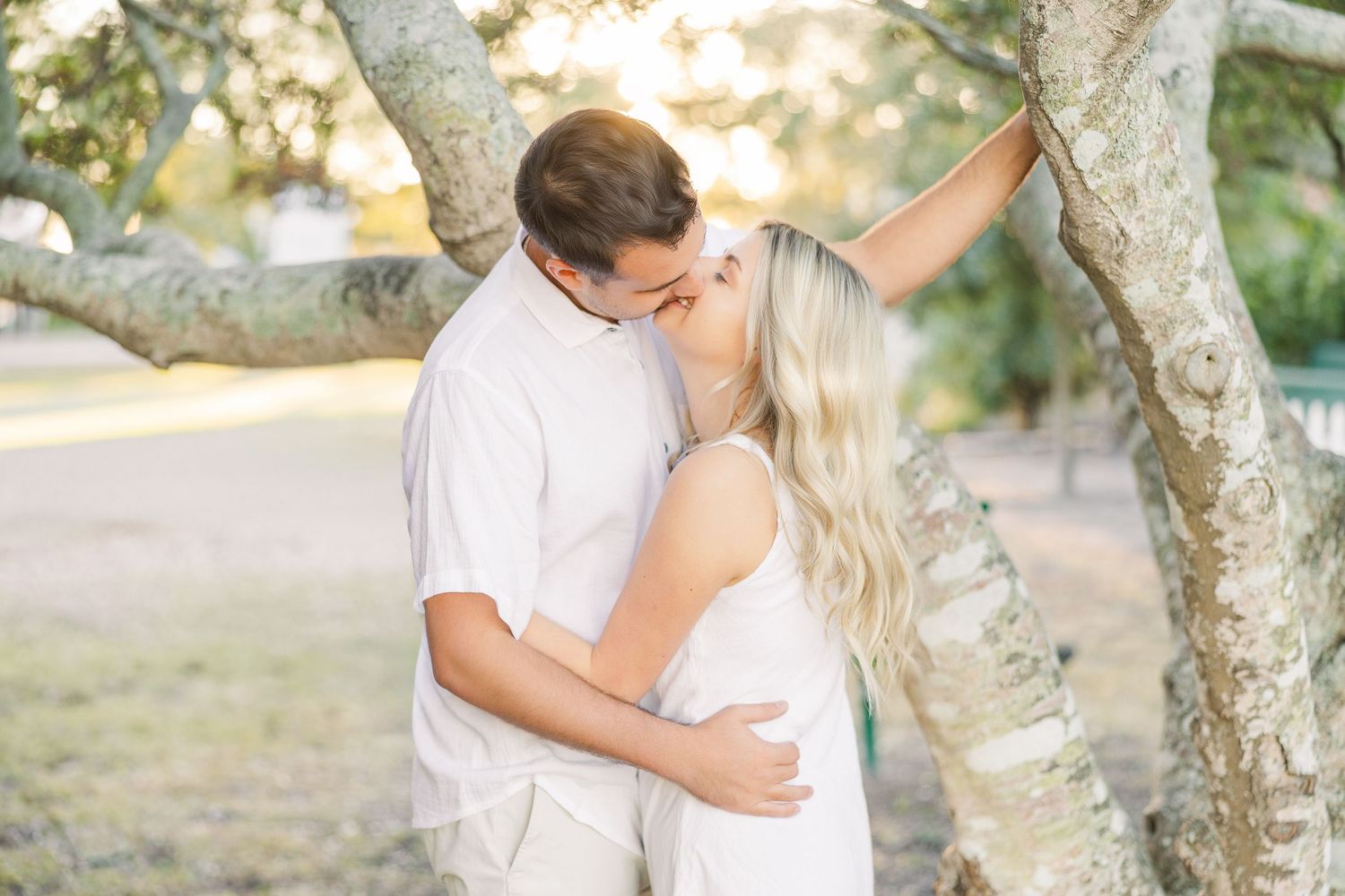 Couple embracing under tree branches during sunset engagement photo session.